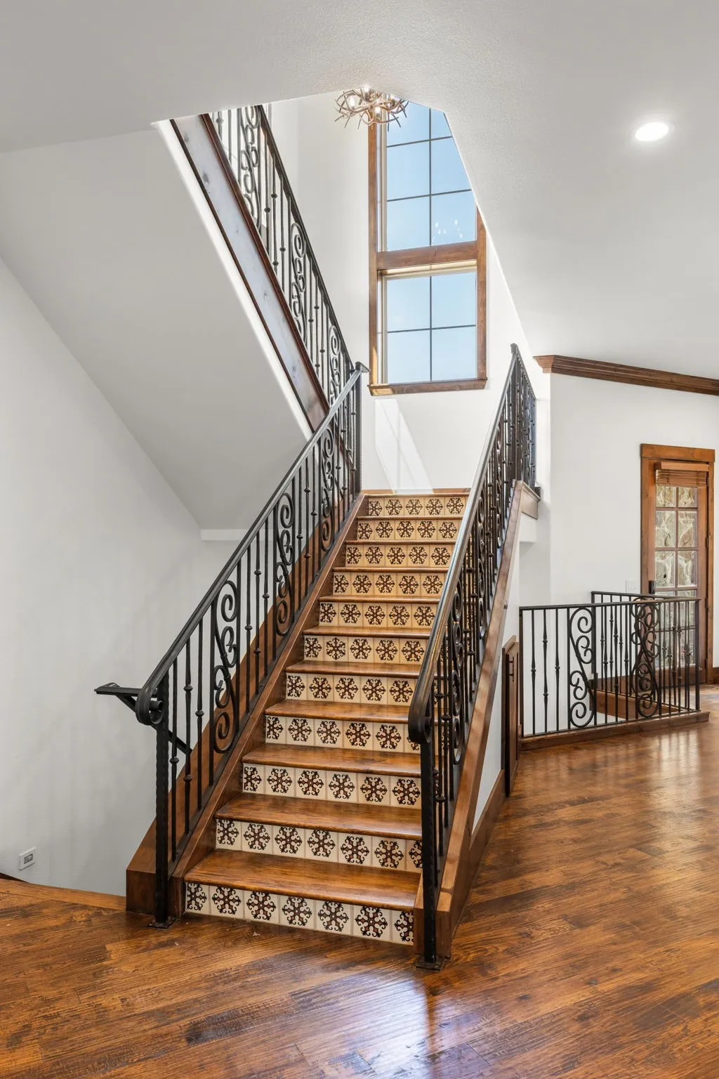 Grand staircase featuring ornate wrought iron railings, patterned risers, and rich wood treads