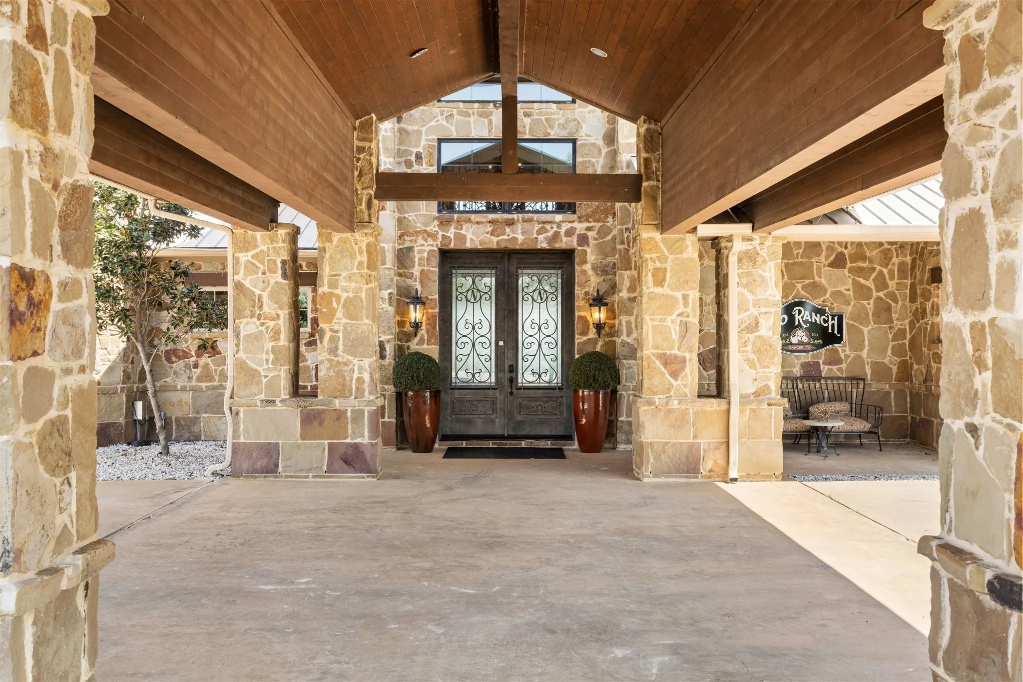 Stone masonry facade featuring a covered entry, wood-finish ceiling, double entry doors with decorative ironwork, and exterior lighting fixtures