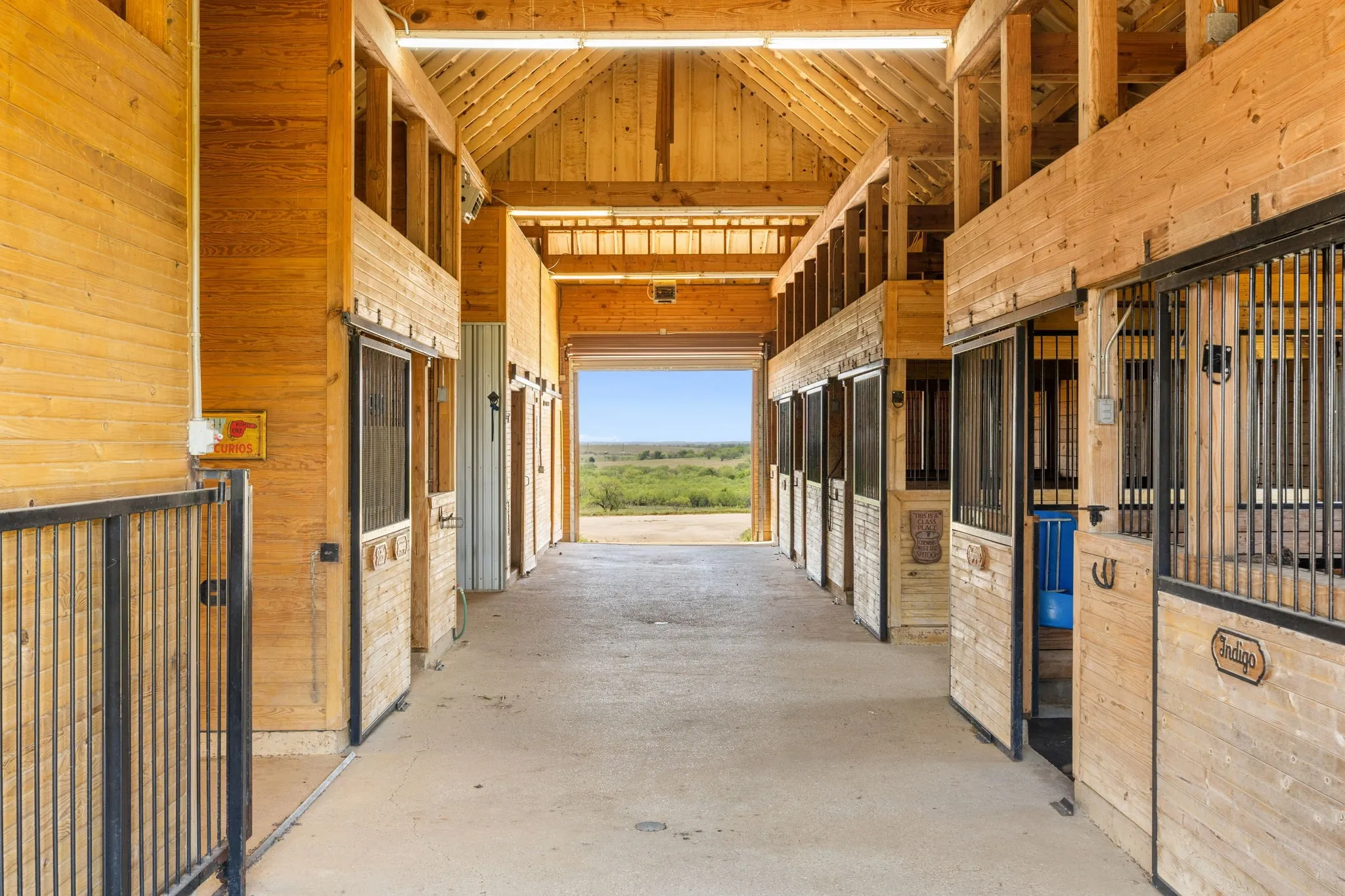 Barn interior featuring multiple stalls with wood-finish walls and black metal grating