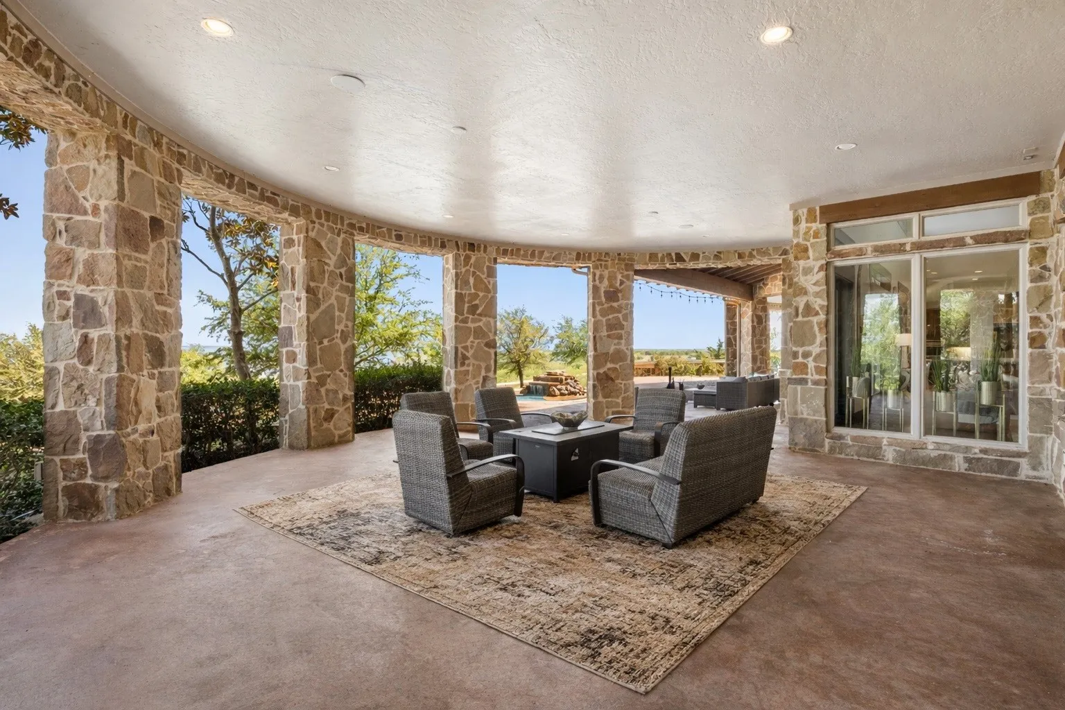 Curved covered patio featuring stone columns and a concrete floor