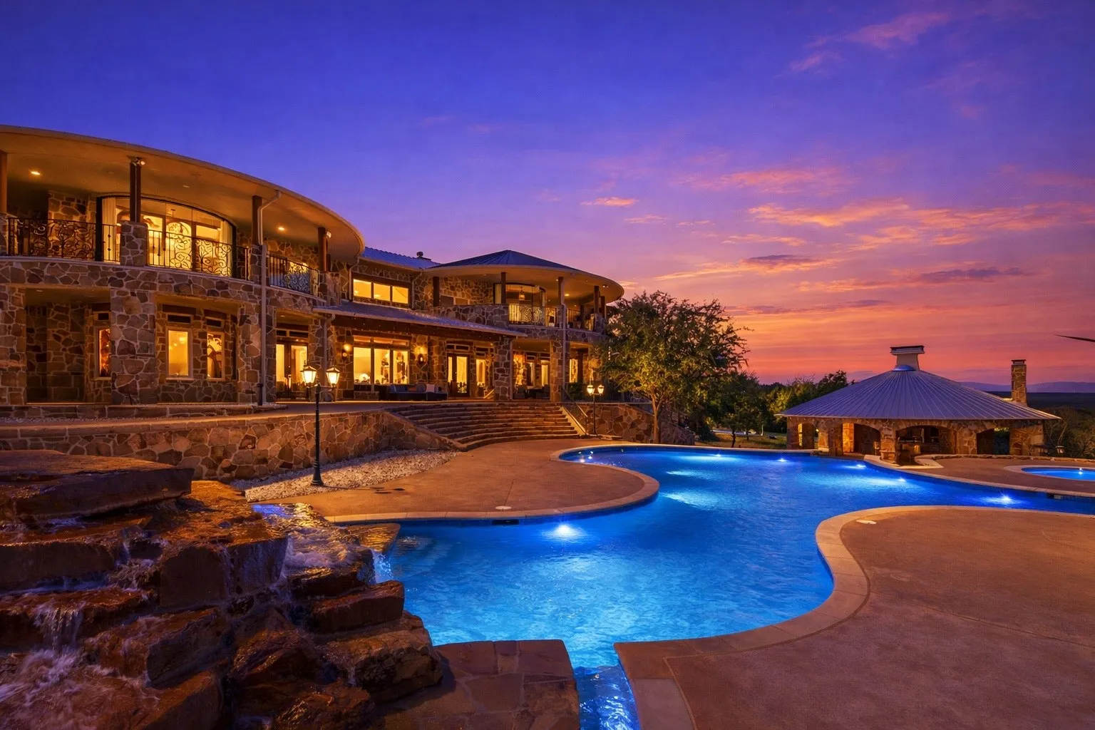 Expansive multi-level custom stone exterior residence with an integrated resort-style pool and rock waterfall feature