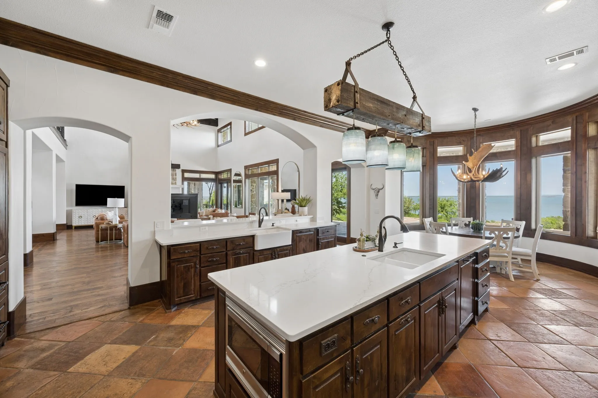 Spacious kitchen featuring a large central island with white countertop and integrated sink, rich wood cabinetry, and a beamed ceiling detail