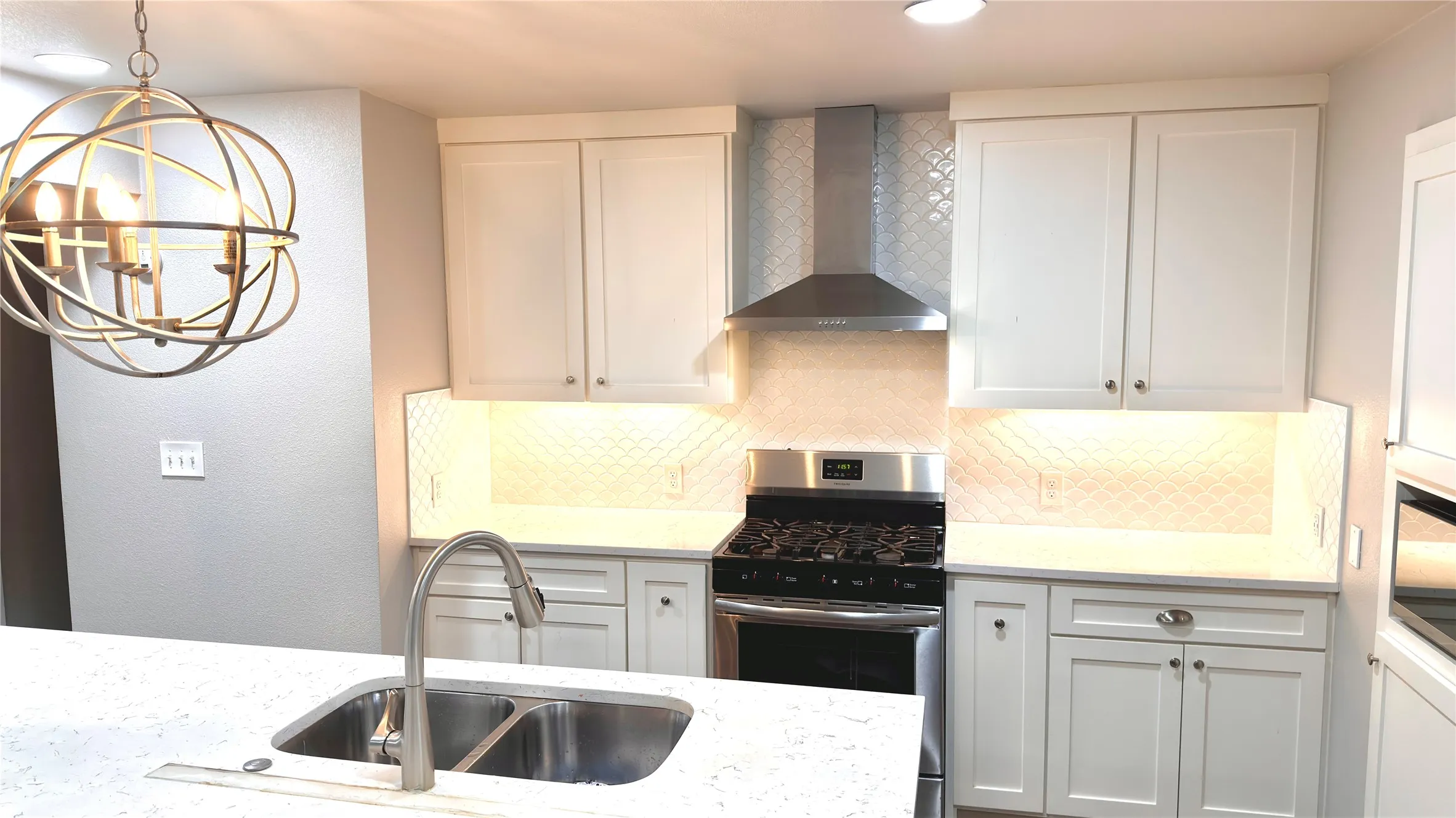 Kitchen featuring stainless steel range with gas stovetop, wall chimney range hood, hanging light fixtures, tasteful backsplash, and light stone counters
