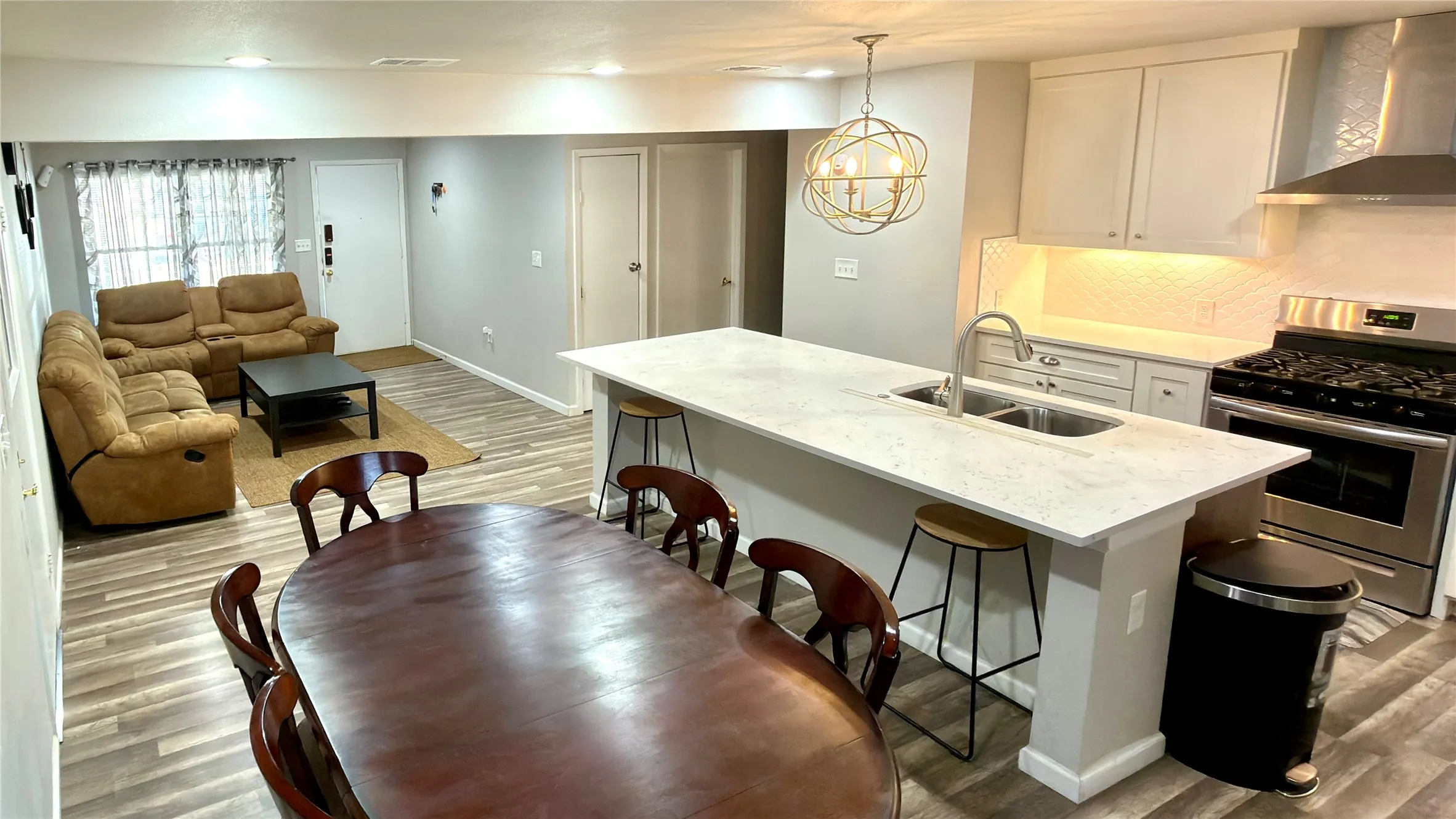 Kitchen with stainless steel gas stove, wall chimney exhaust hood, light wood finished floors, tasteful backsplash, and white cabinets