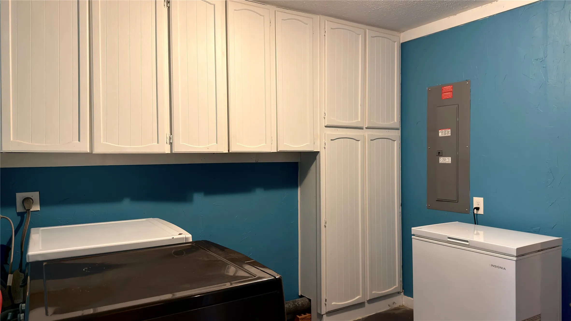 Washroom featuring electric panel, a textured ceiling, cabinet space, and washer and dryer
