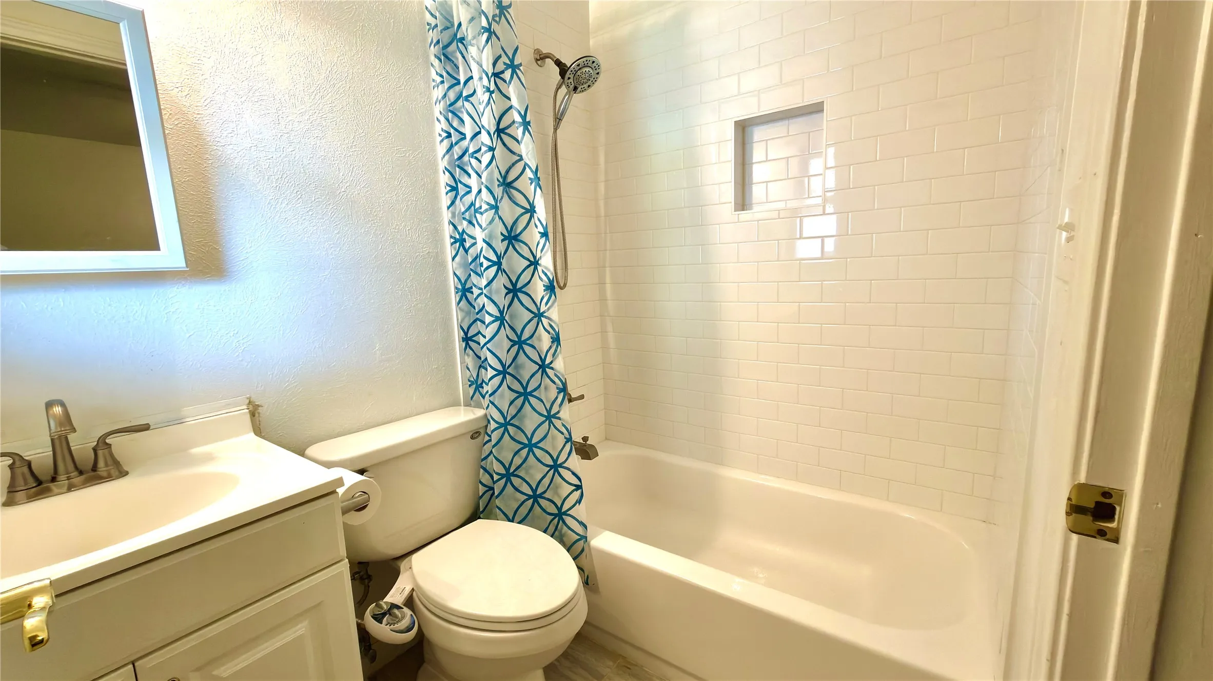 Bathroom with a textured wall, vanity, and shower / tub combo with curtain