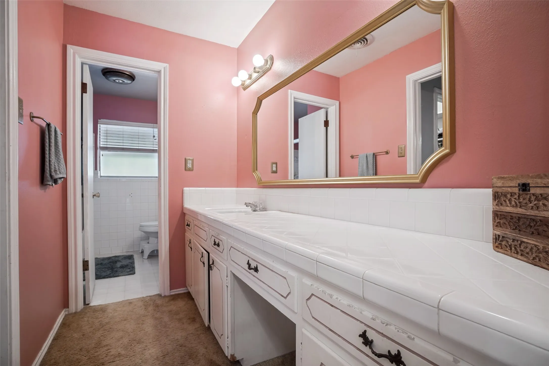 Vanity with a tiled countertop, gold-framed mirror, and integrated sink