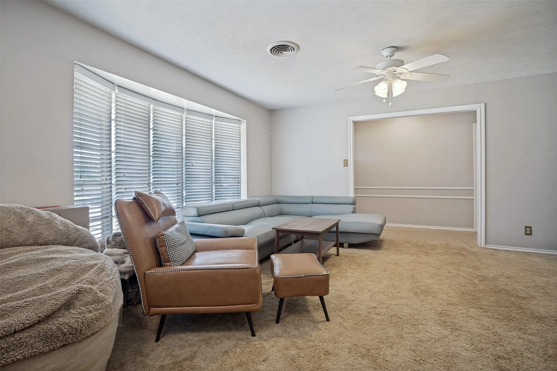 Carpeted living area with a large bay window featuring horizontal blinds