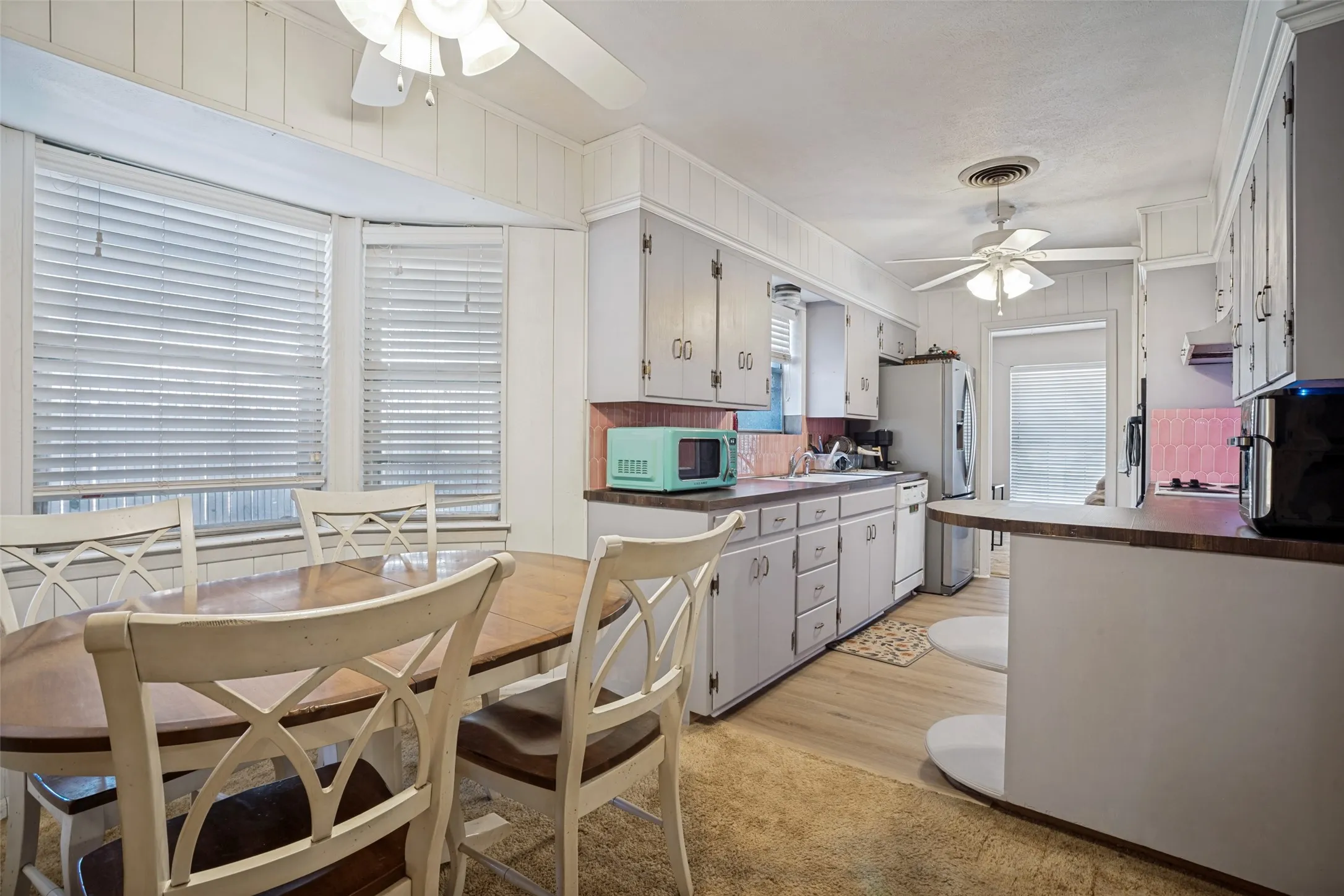 Kitchen featuring light-toned cabinetry, wood-finish flooring, a built-in breakfast bar, and a bay window