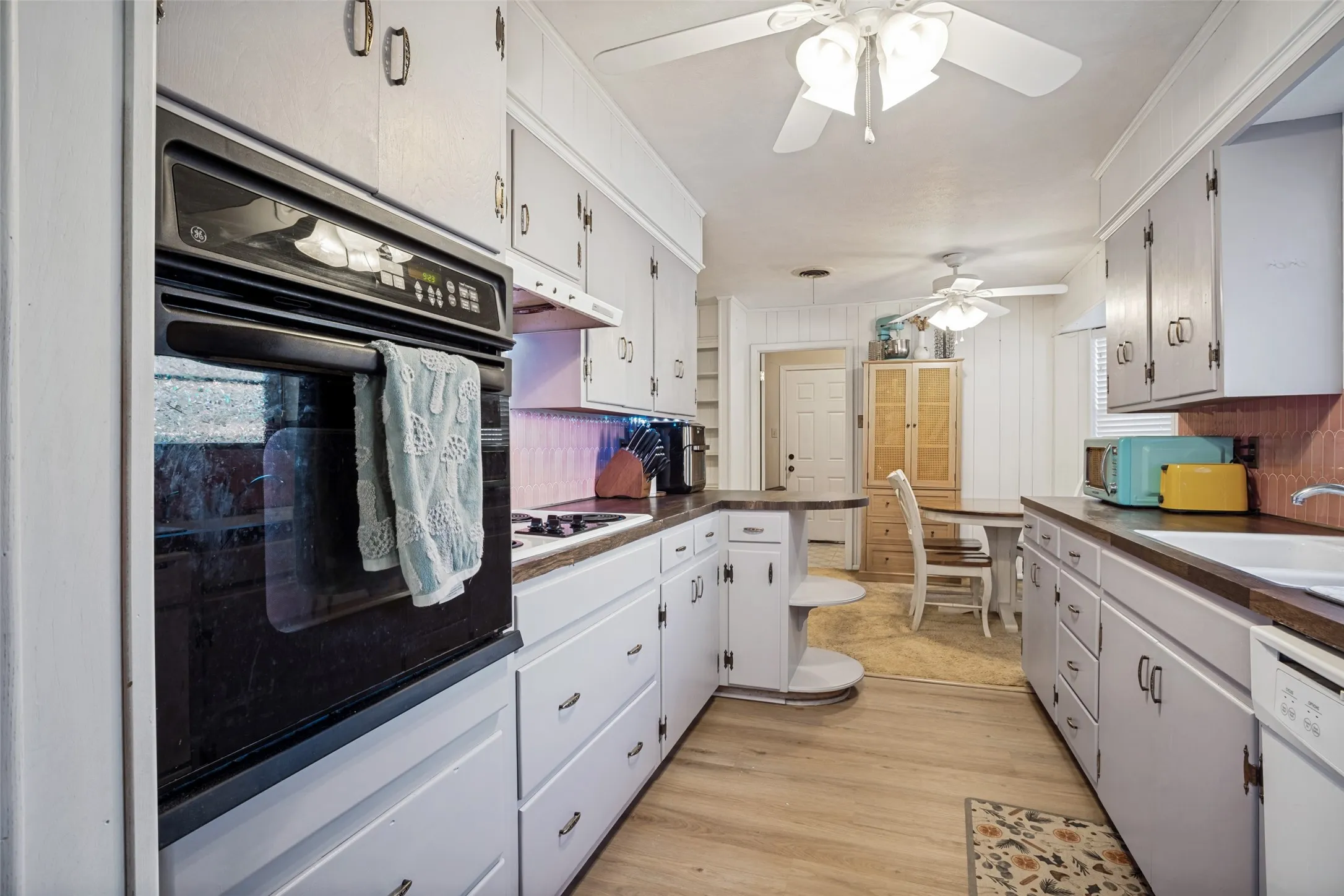 Galley kitchen featuring a built-in wall oven, gas cooktop, wood-finish flooring, white cabinetry, and a ceiling fan