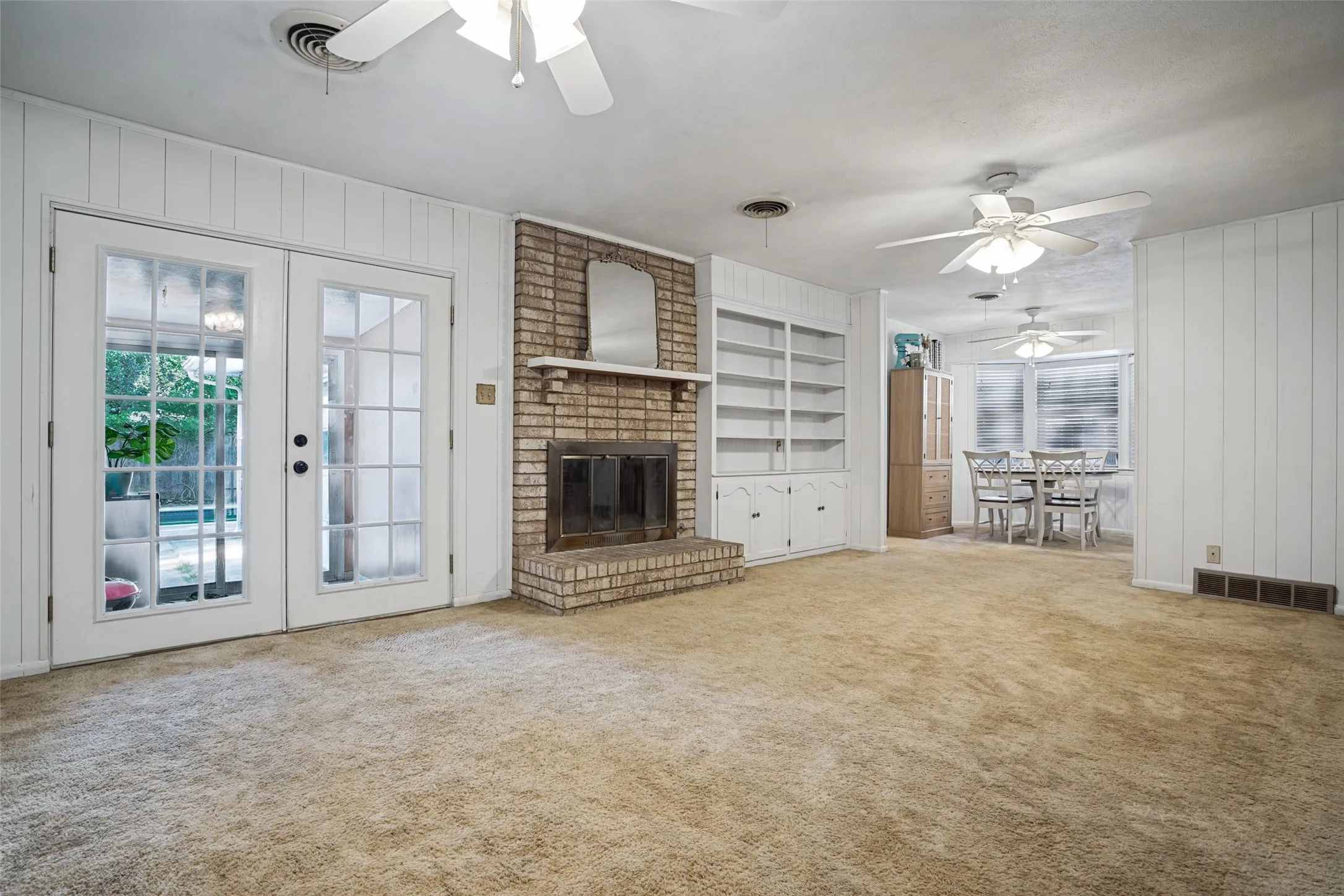 Brick fireplace with a hearth, built-in shelving, and French doors