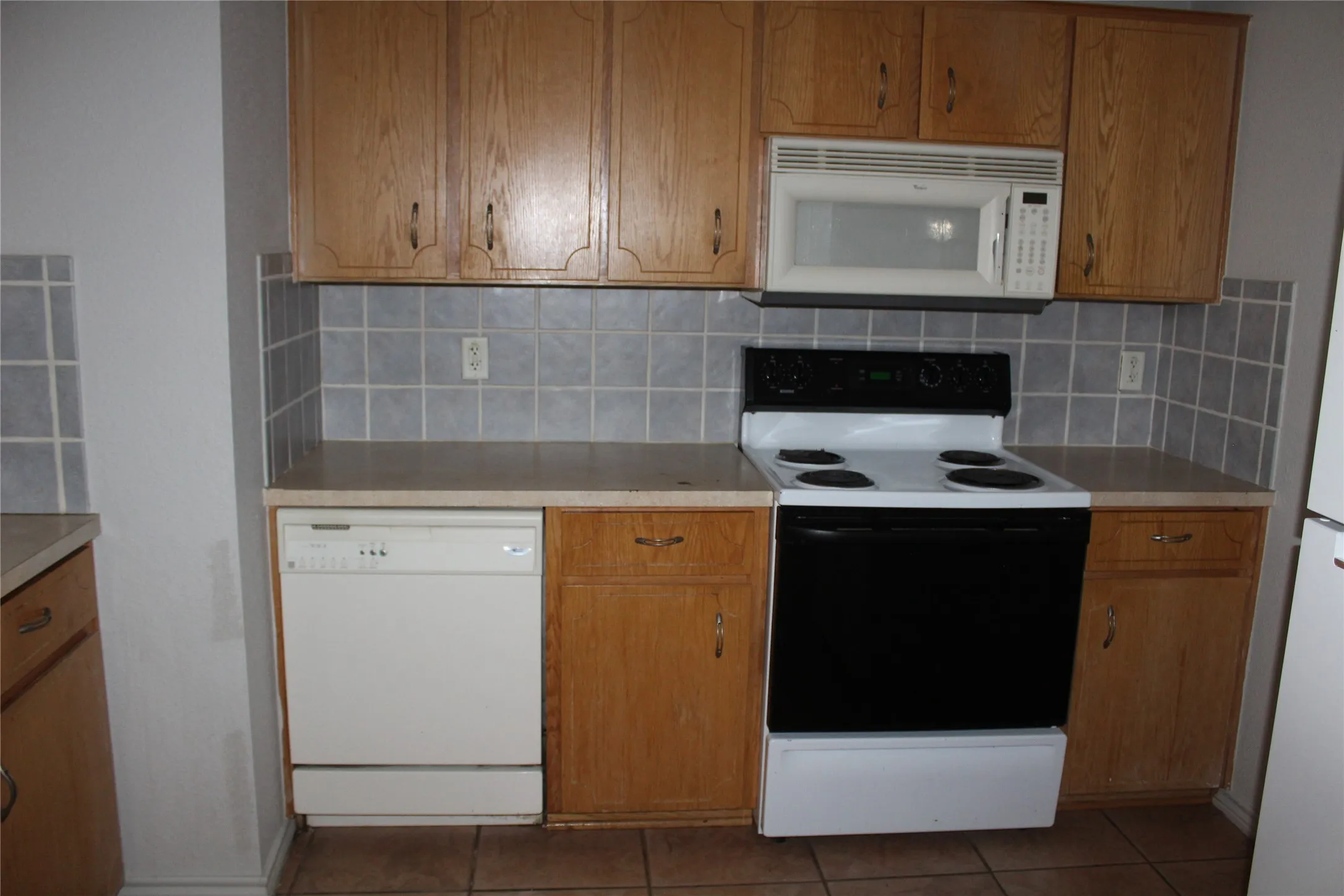 Kitchen with white appliances, brown cabinetry, light countertops, tile patterned flooring, and tasteful backsplash