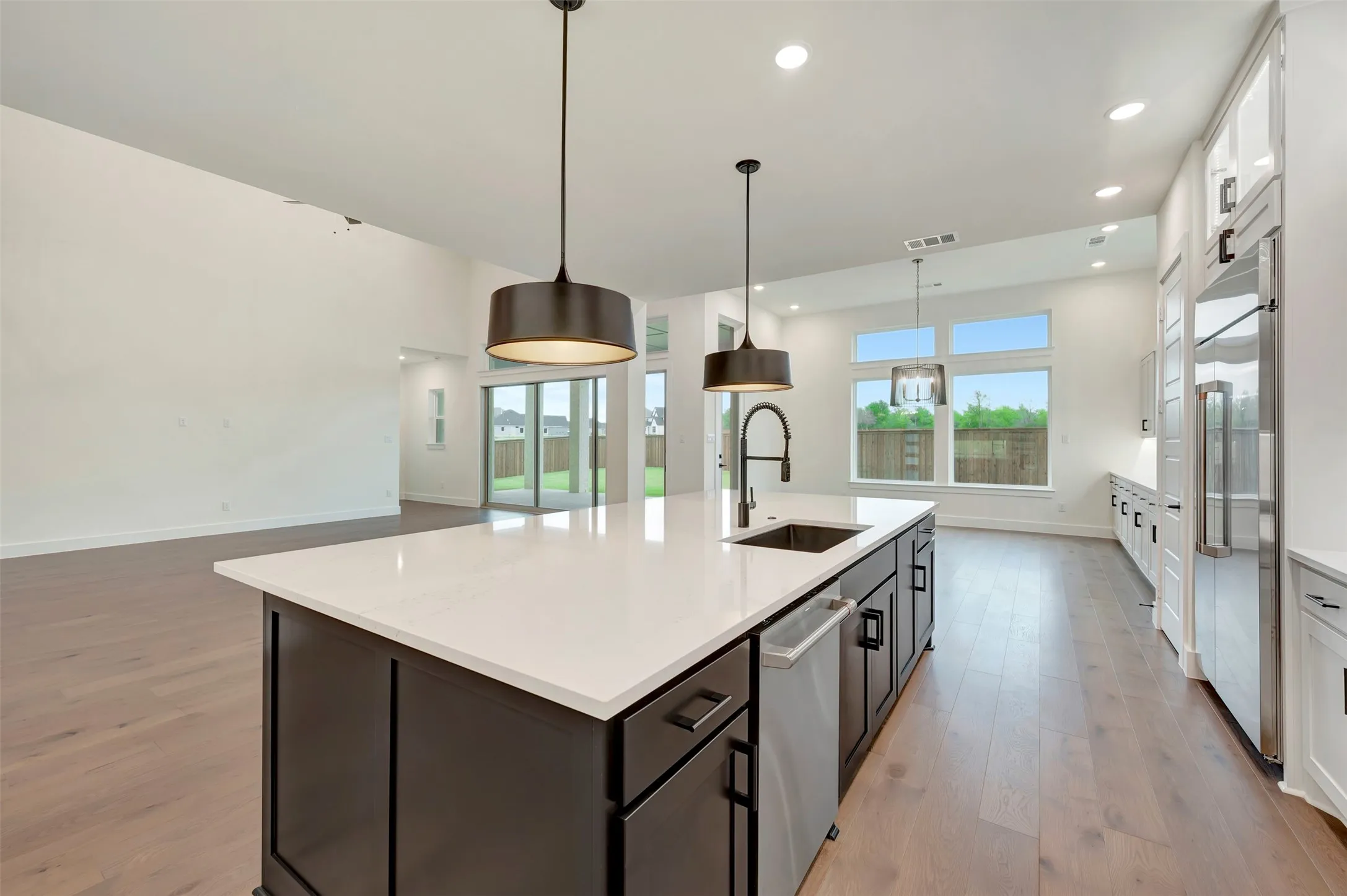 Kitchen with dual tone cabinetry, pendant lighting, light wood-style flooring, a center island with sink, and stainless steel appliances