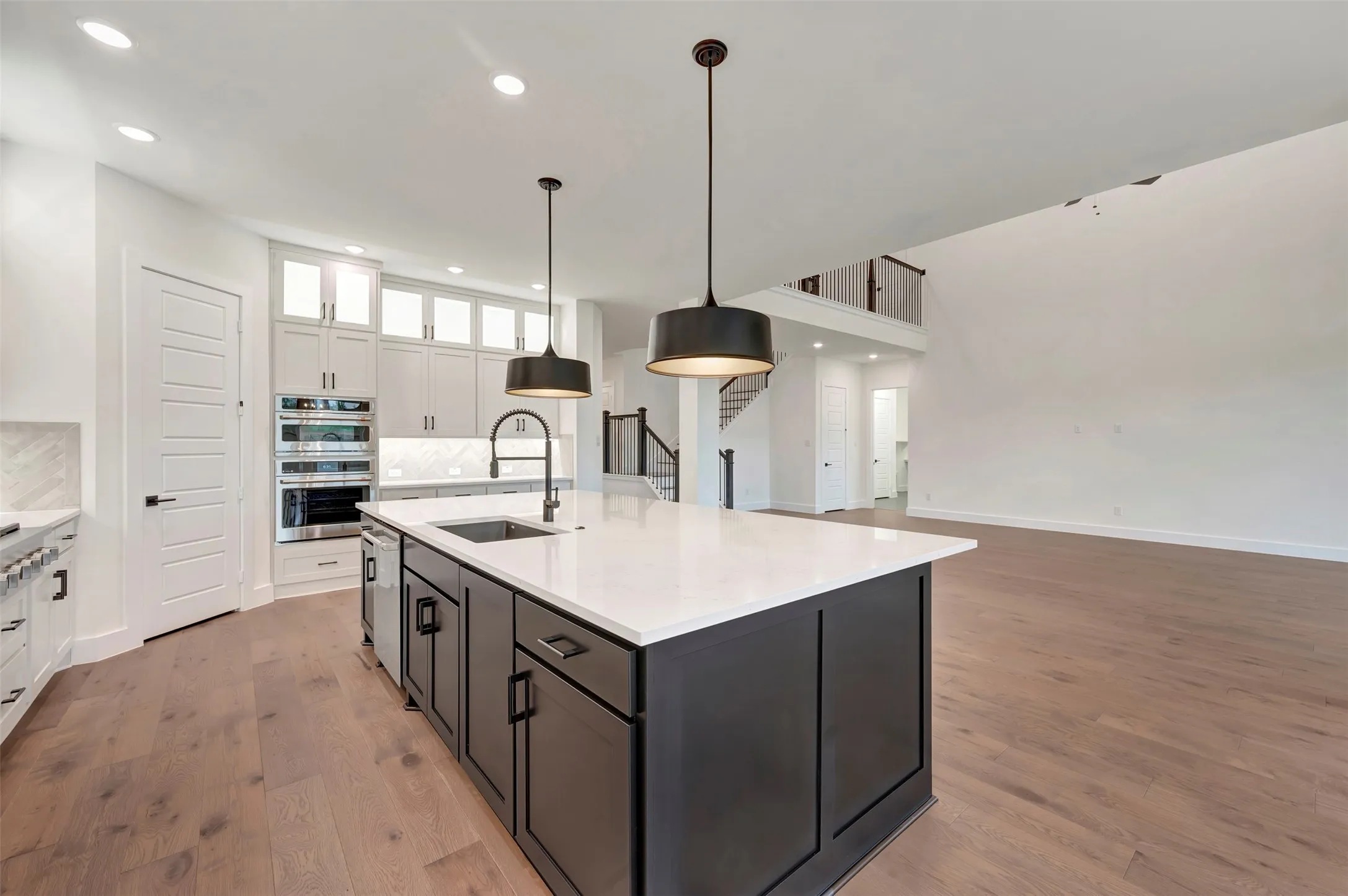 Kitchen with hanging light fixtures, light stone counters, dual tone cabinetry, light wood-style floors, and glass fronted cabinets
