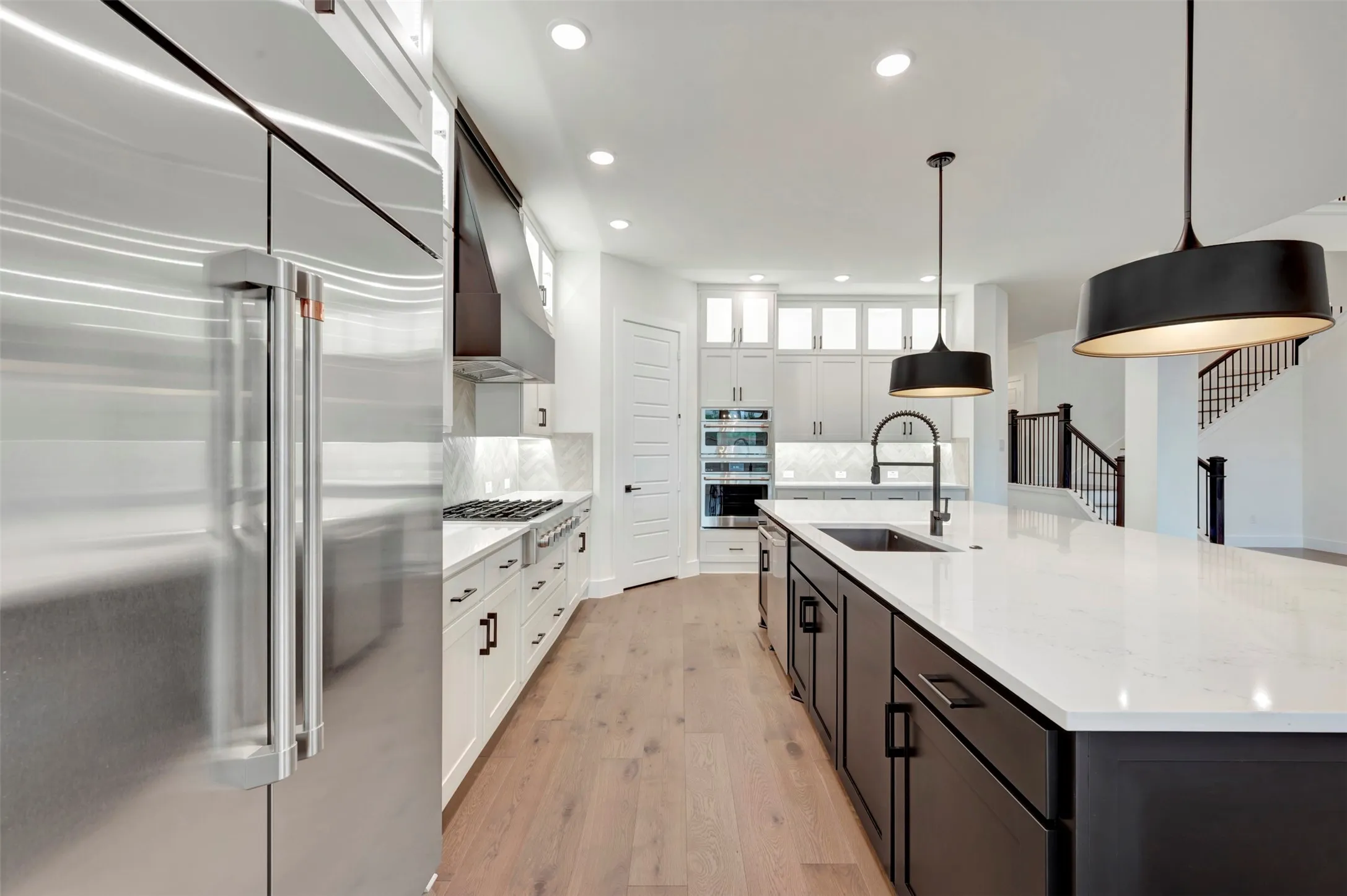 Dual tone kitchen with stainless steel appliances, dual tone cabinetry, hanging light fixtures, a large island, and light wood-style flooring