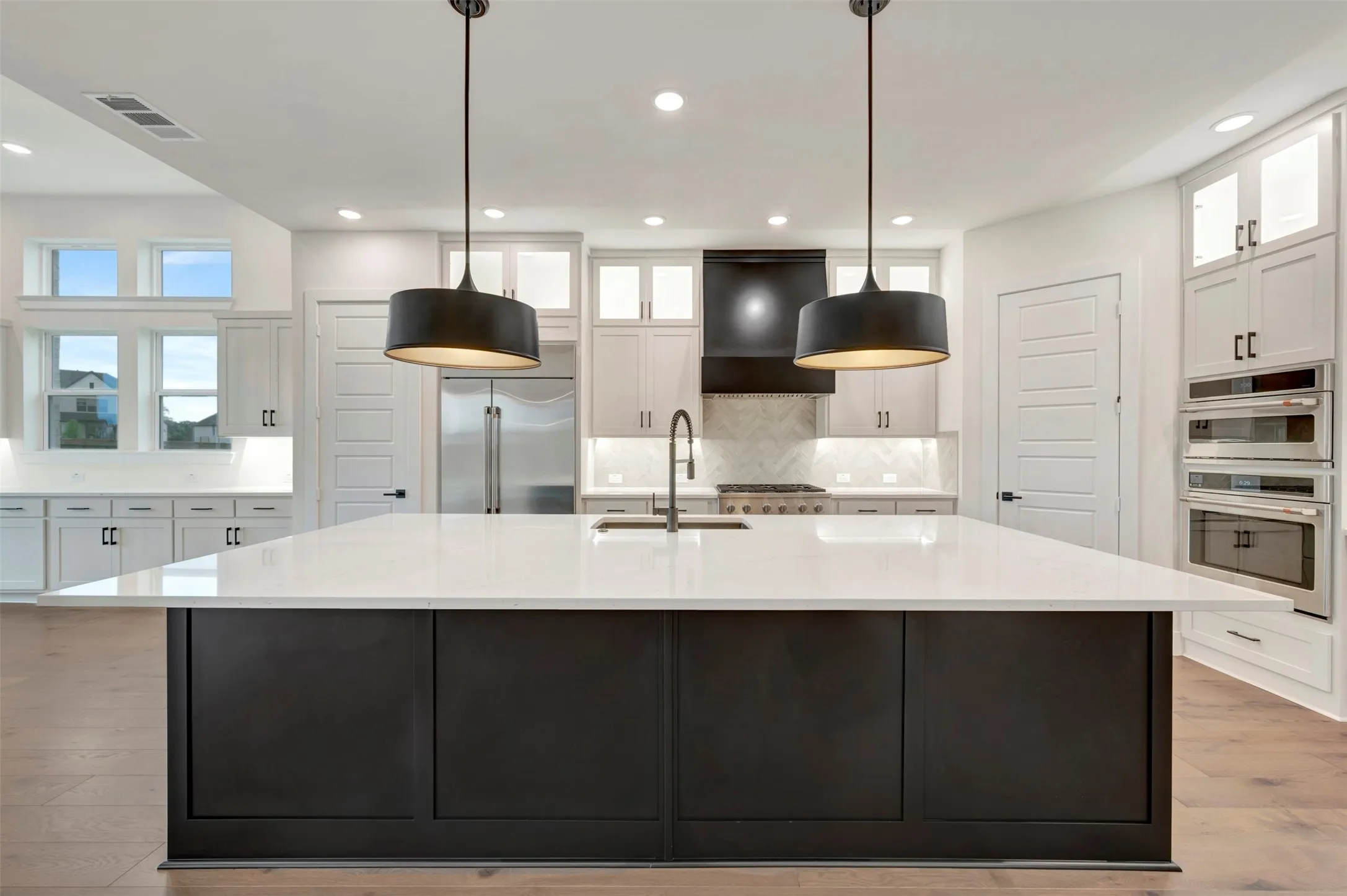 Kitchen with dual tone cabinets, a large island, light wood finished floors, glass fronted cabinets, and pendant lighting