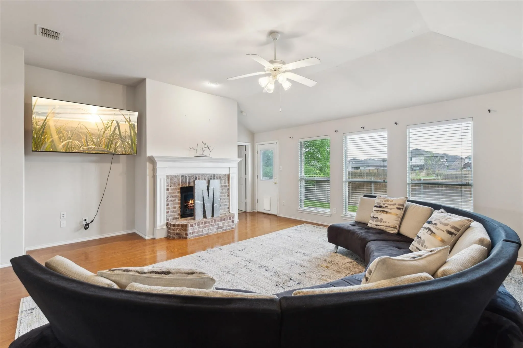 Living room with lofted ceiling, light wood-style floors, a fireplace, and ceiling fan
