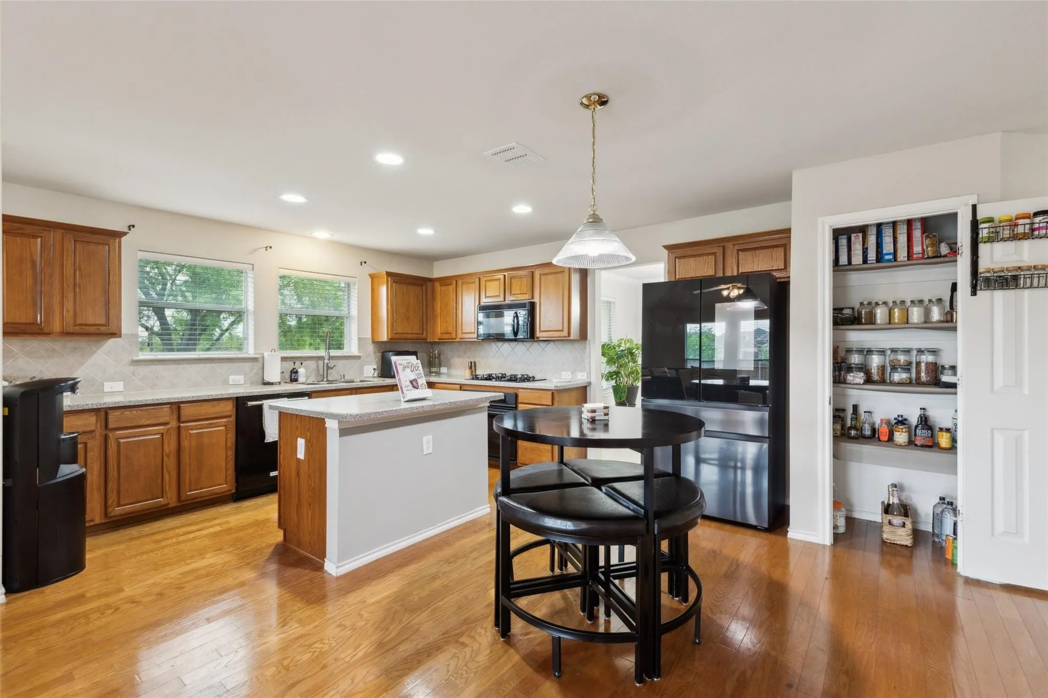 Kitchen featuring brown cabinets, tasteful backsplash, light wood finished floors, black appliances, and recessed lighting