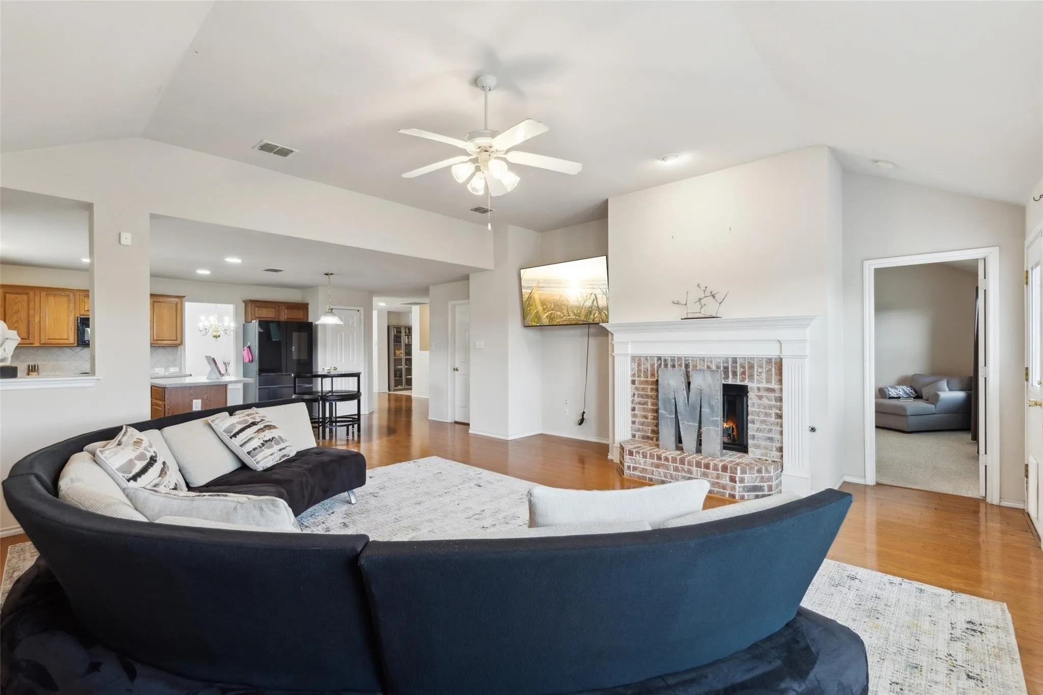 Living area featuring light wood finished floors, ceiling fan, a fireplace, and lofted ceiling