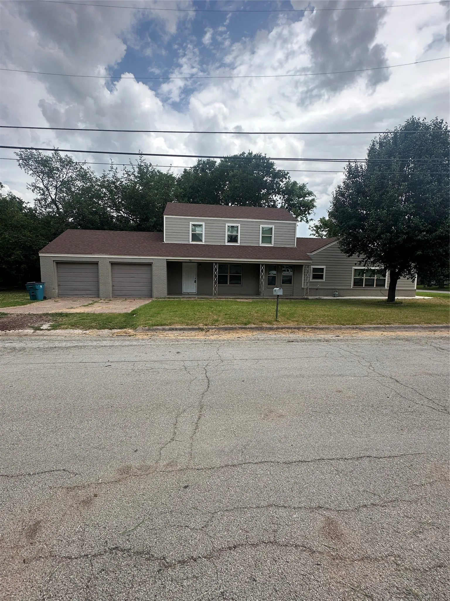 View of front facade featuring a front lawn, a garage, driveway, and a porch