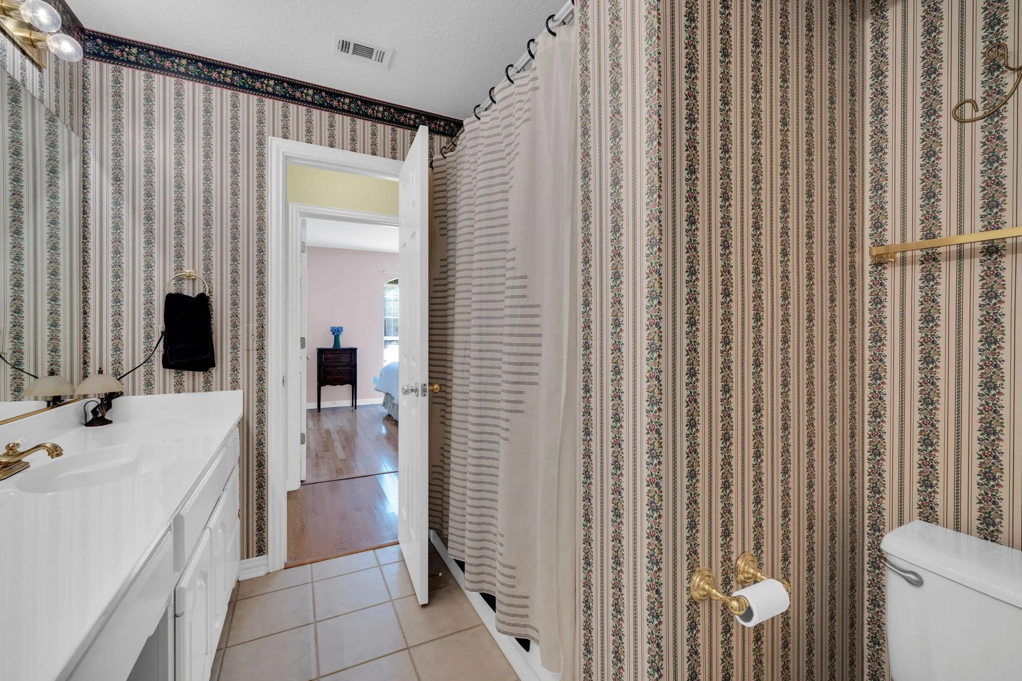 Full bathroom with light tile patterned floors, curtained shower, vanity, and wallpapered walls