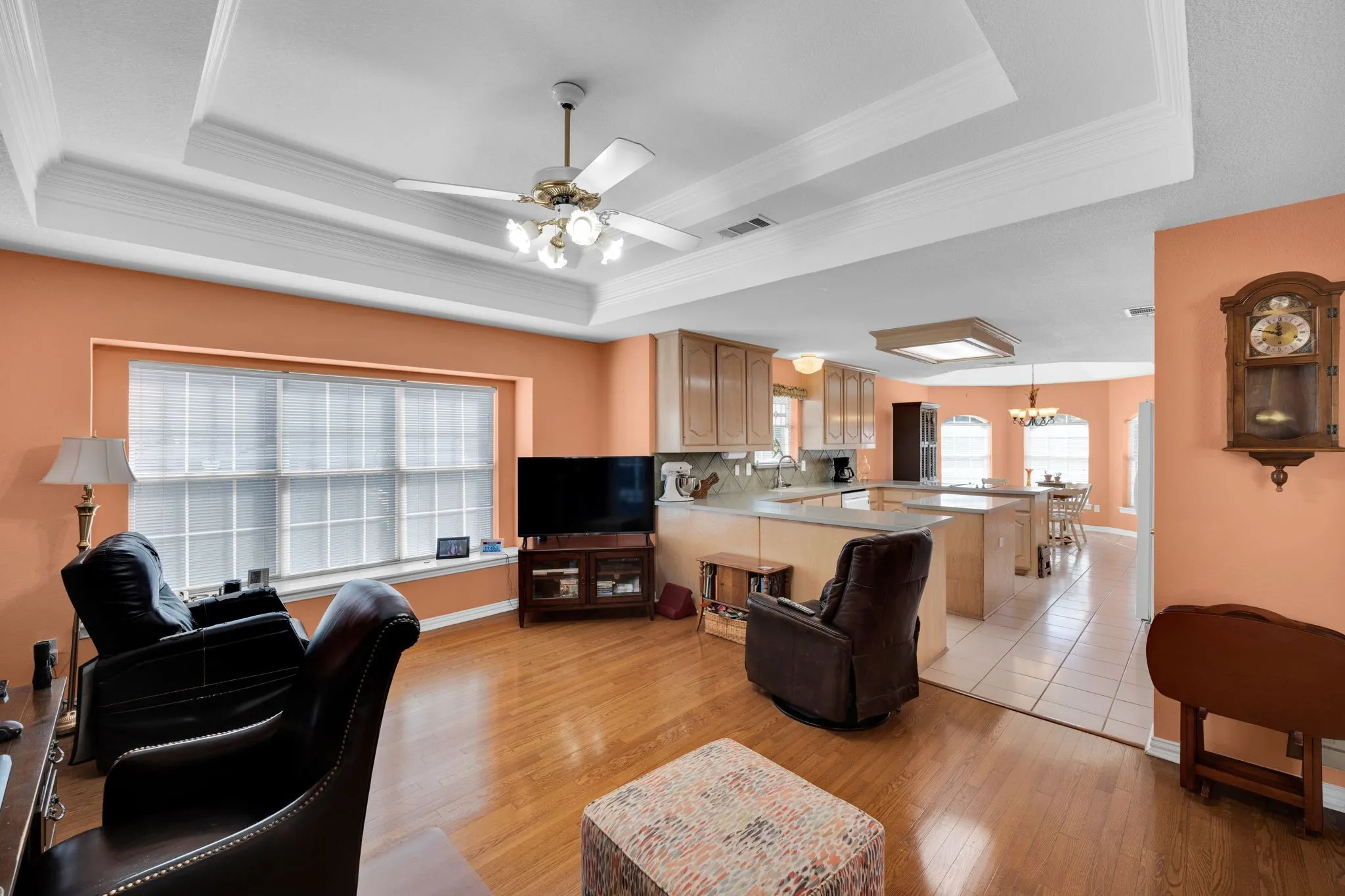Living room with a tray ceiling, light wood-style floors, ceiling fan, a chandelier, and ornamental molding