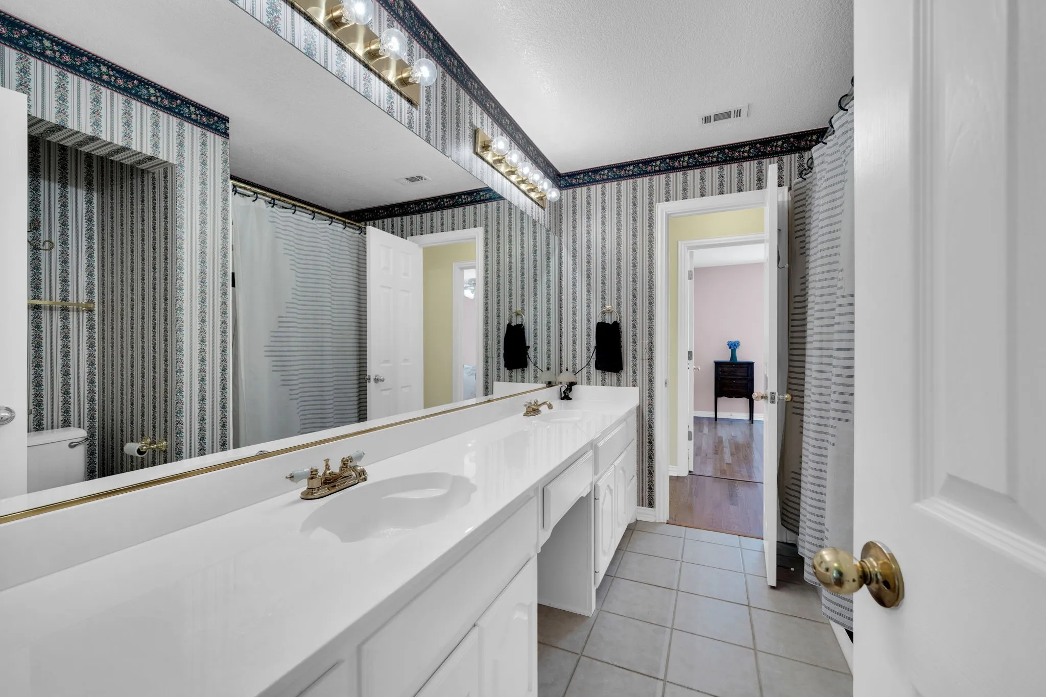 Full bathroom with double vanity, light tile patterned floors, wallpapered walls, and a shower with shower curtain