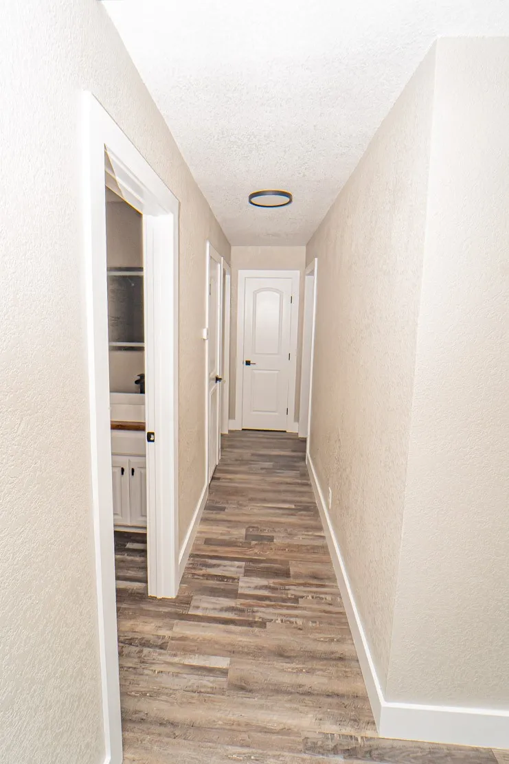 Corridor featuring a textured wall, light wood finished floors, and a textured ceiling