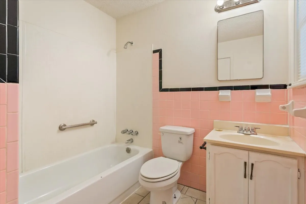 Bathroom with tile walls, vanity, light tile patterned flooring, washtub / shower combination, and a textured ceiling