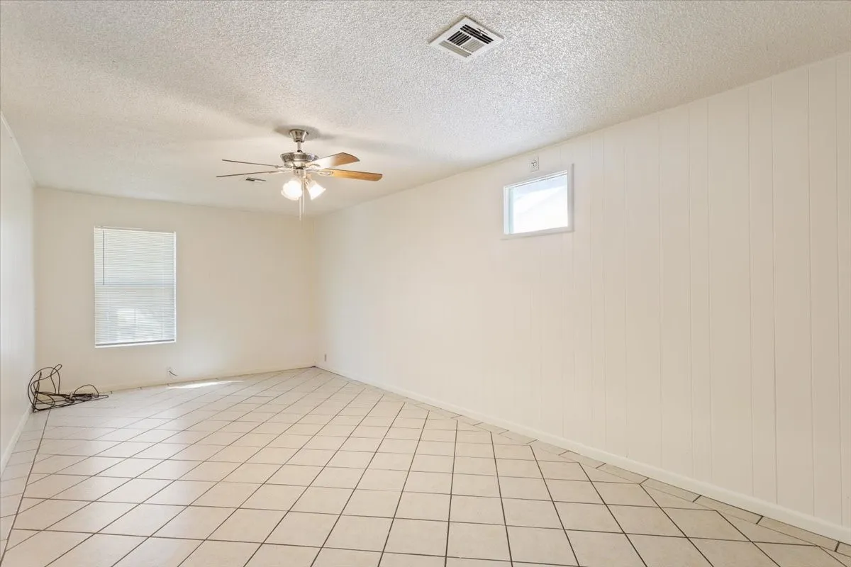 Empty room with a textured ceiling, ceiling fan, and light tile patterned floors