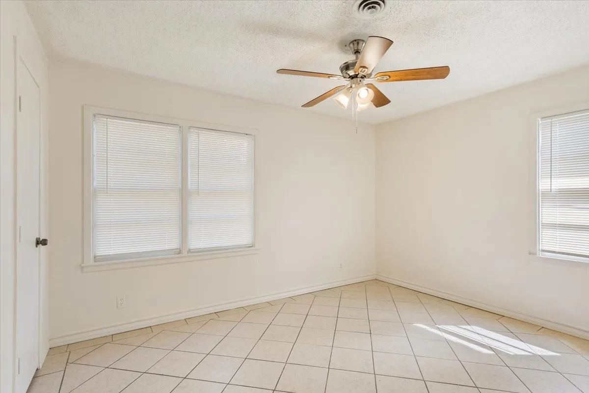 Spare room with a textured ceiling, light tile patterned floors, healthy amount of natural light, and a ceiling fan