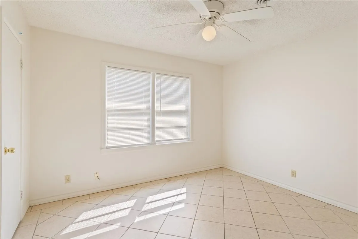 Unfurnished room with a textured ceiling, light tile patterned floors, and a ceiling fan