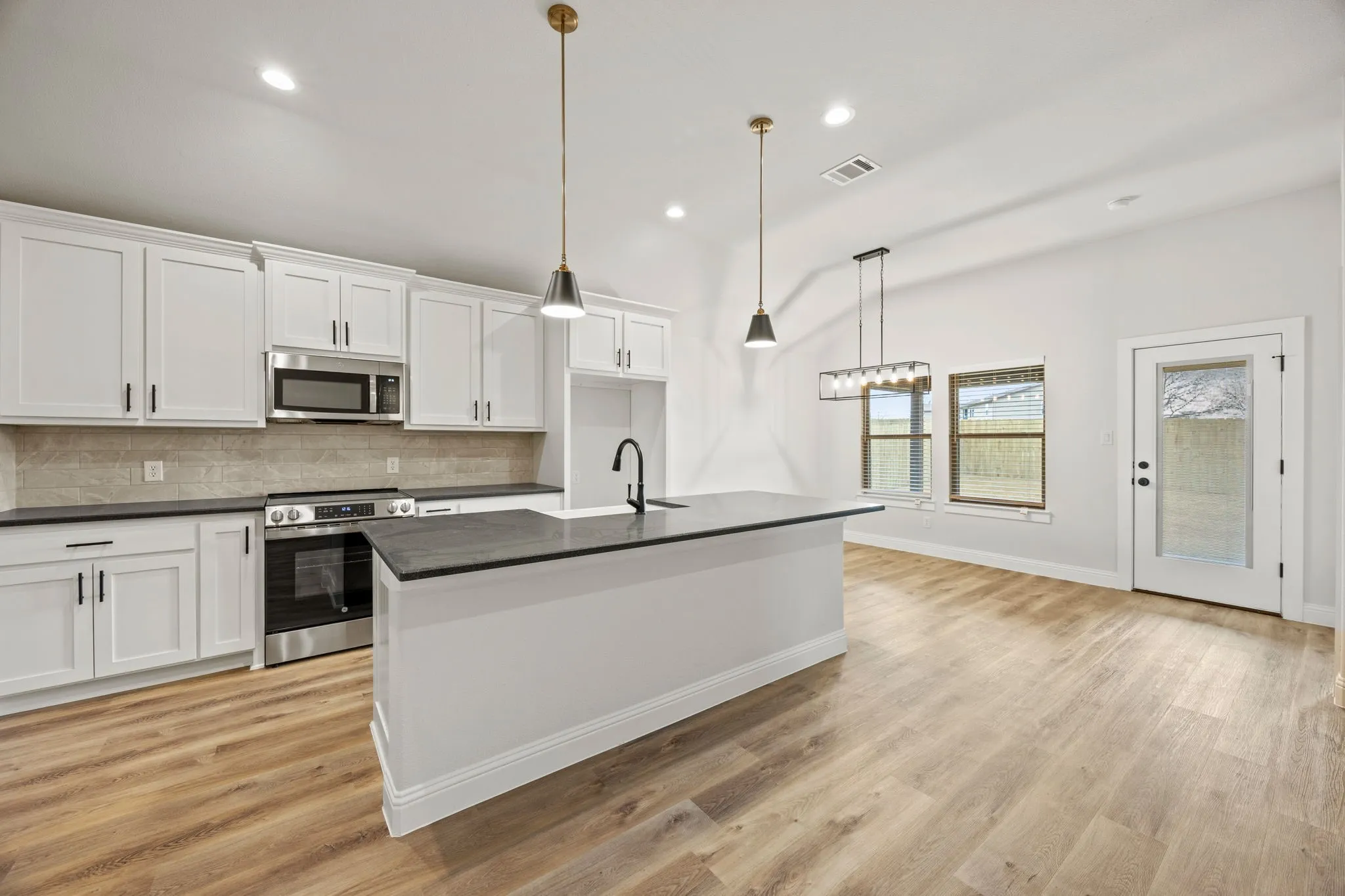 Kitchen with appliances with stainless steel finishes, an island with sink, backsplash, white cabinets, and recessed lighting