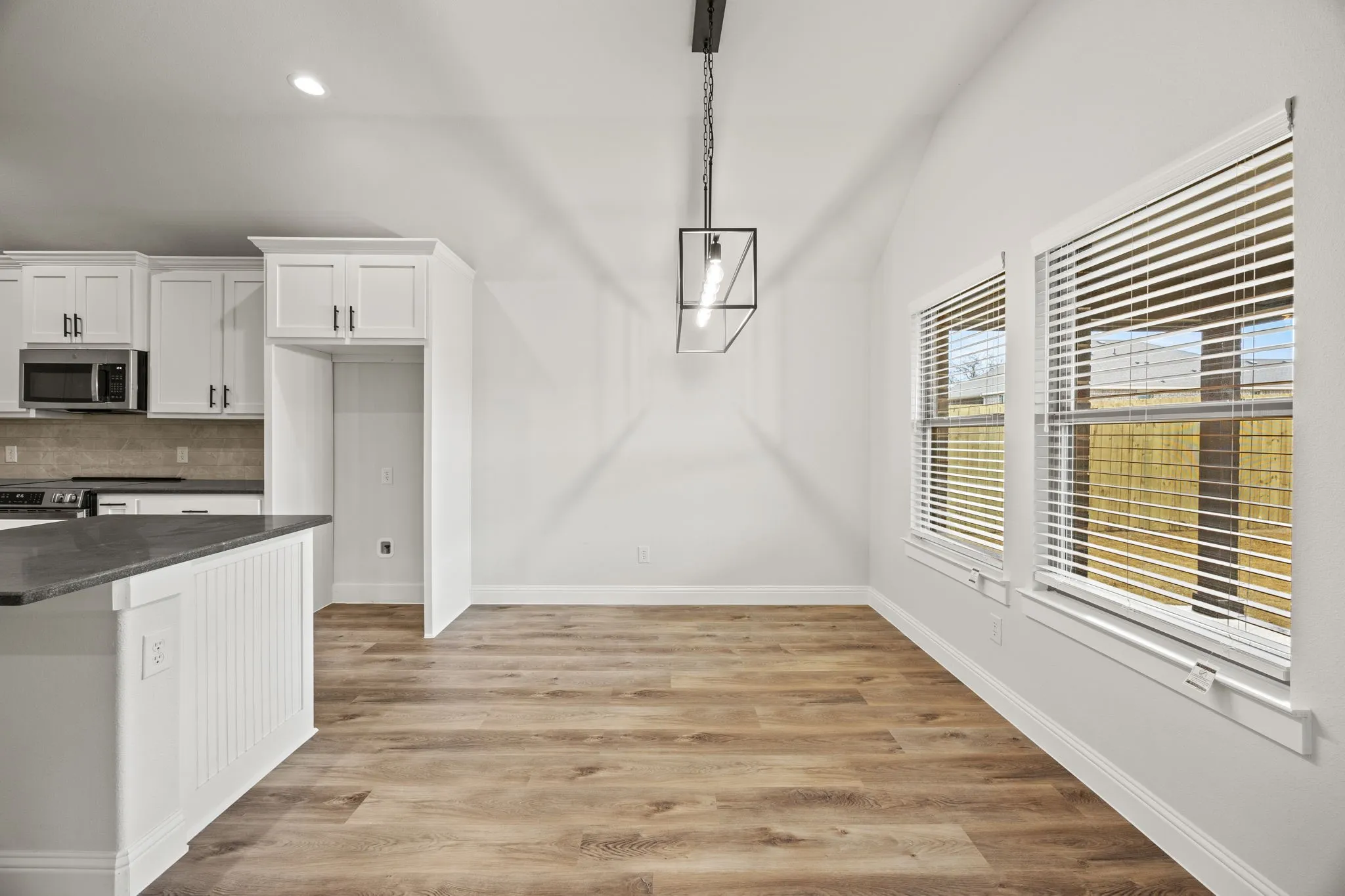 Kitchen with white cabinetry, backsplash, vaulted ceiling, light wood-style flooring, and dark stone counters