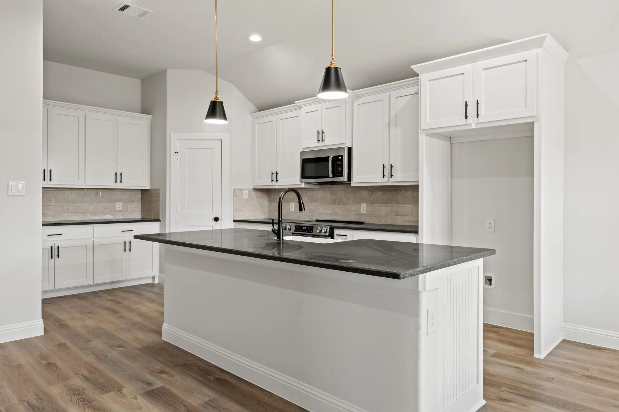 Kitchen featuring white cabinetry, a center island with sink, appliances with stainless steel finishes, hanging light fixtures, and vaulted ceiling