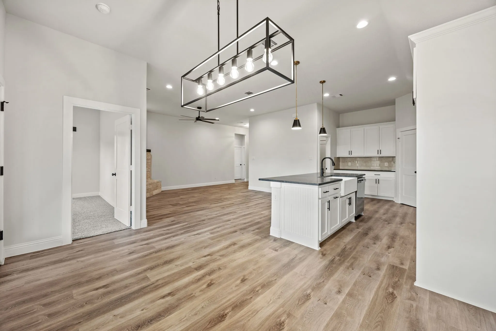 Kitchen with white cabinetry, open floor plan, hanging light fixtures, a kitchen island with sink, and light wood-style flooring