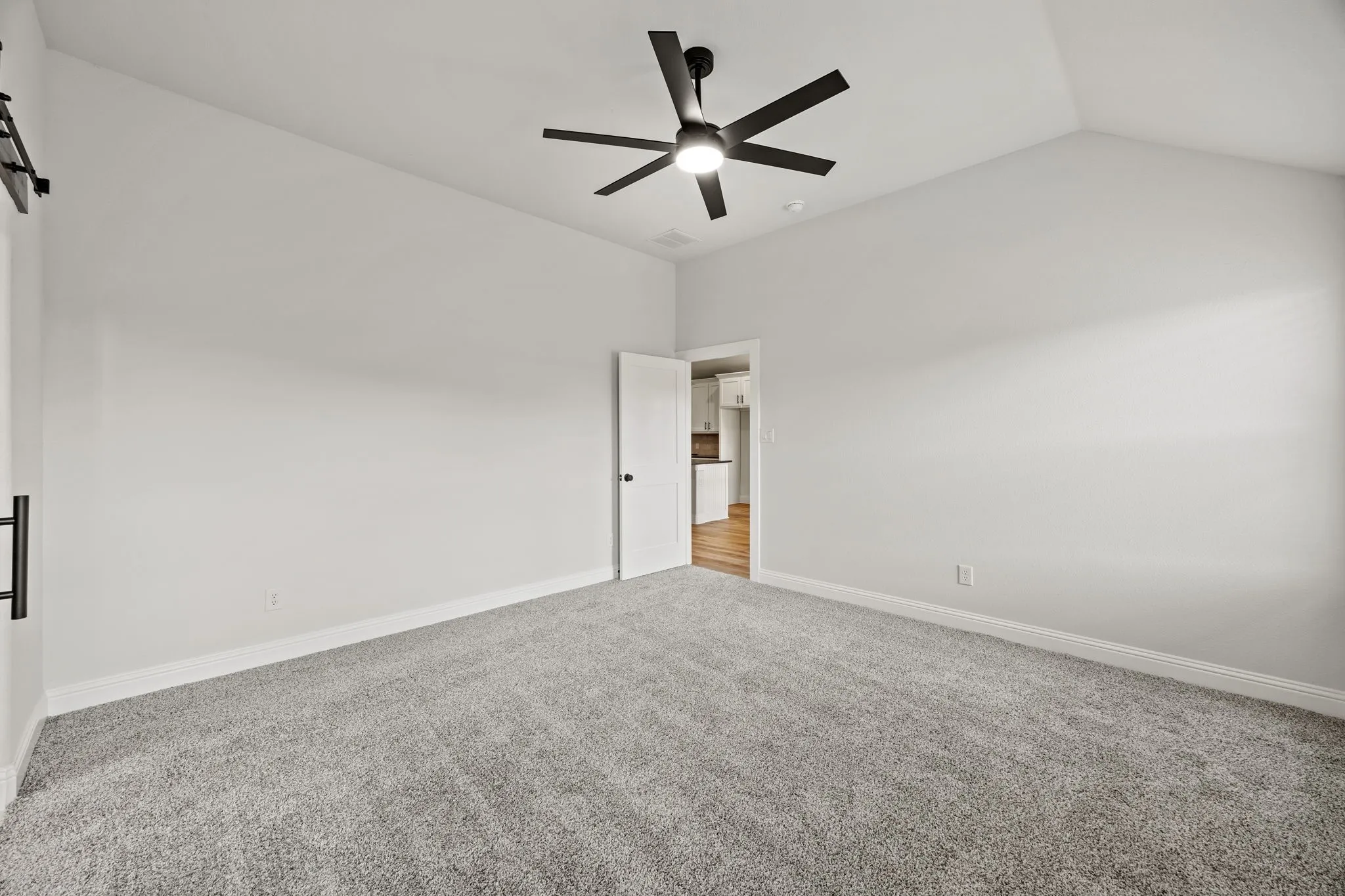 Spare room with light colored carpet, vaulted ceiling, a ceiling fan, and a barn door