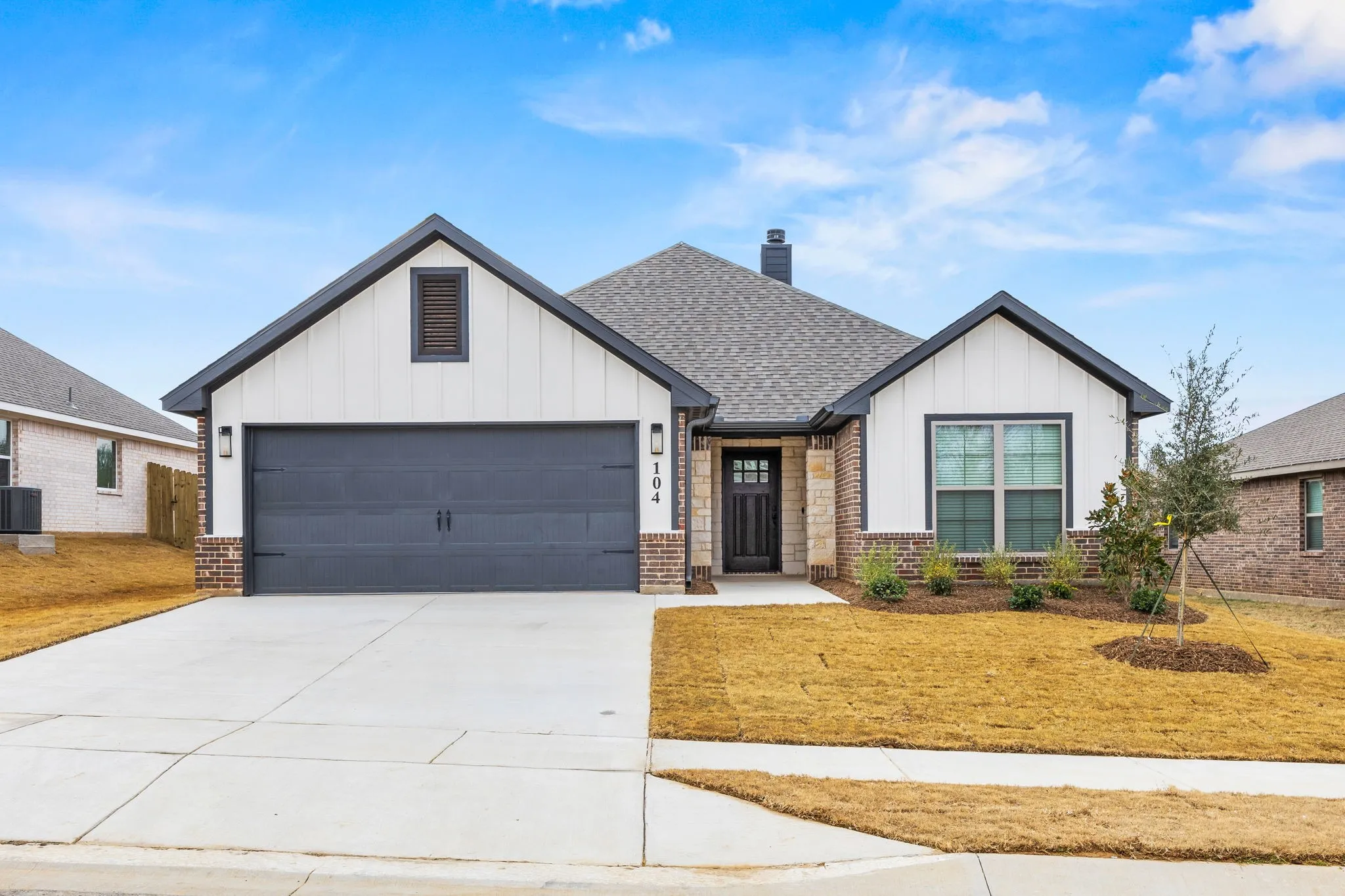 Modern farmhouse style home featuring board and batten siding, driveway, an attached garage, and brick siding