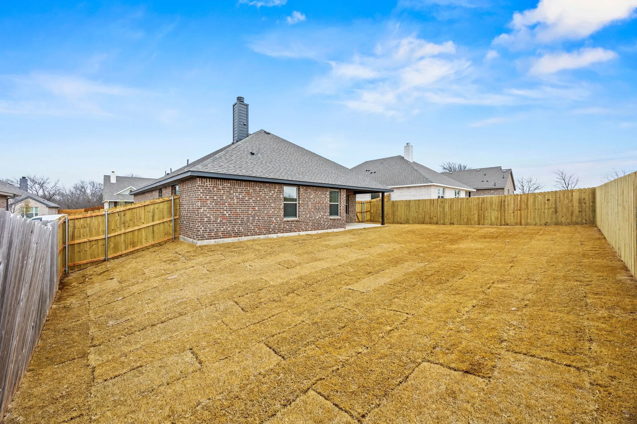 Back of property with brick siding, a fenced backyard, a patio, a chimney, and a shingled roof