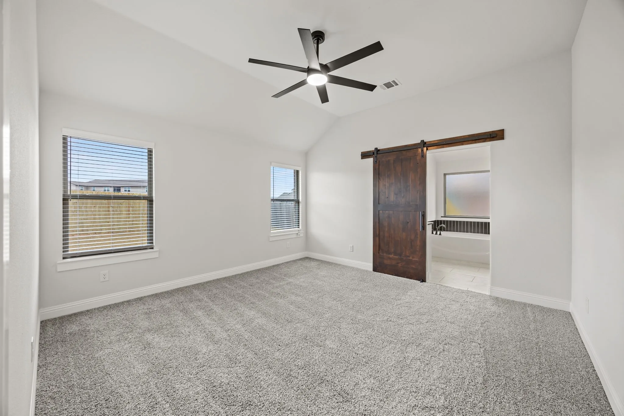 Unfurnished bedroom featuring a barn door, carpet, ceiling fan, and vaulted ceiling