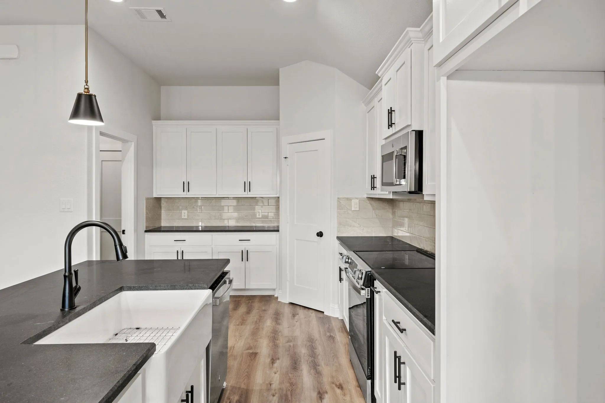 Kitchen with white cabinetry, stainless steel appliances, decorative light fixtures, light wood-type flooring, and dark stone countertops