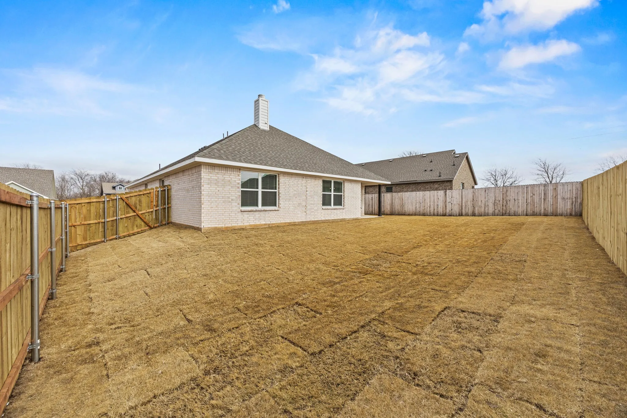 Back of property featuring a chimney, a fenced backyard, a shingled roof, and brick siding
