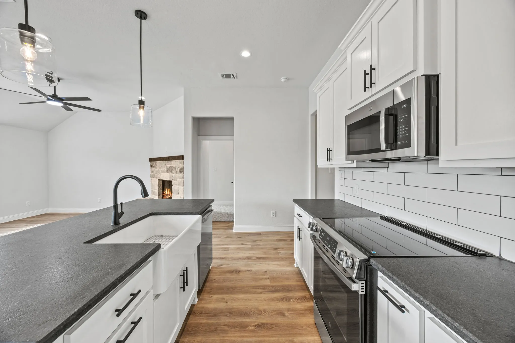 Kitchen with stainless steel appliances, white cabinetry, light wood-type flooring, a stone fireplace, and hanging light fixtures