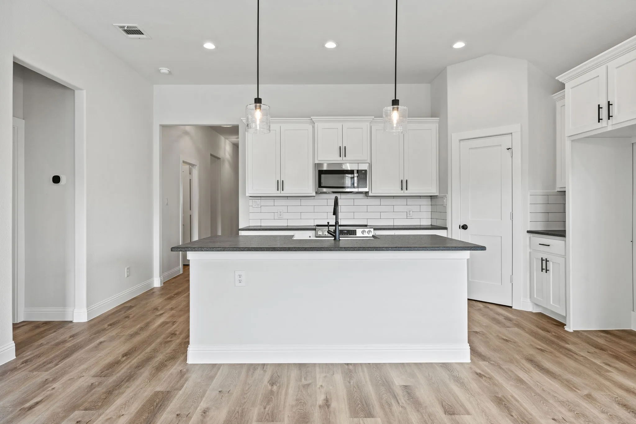 Kitchen with white cabinetry, stainless steel microwave, tasteful backsplash, hanging light fixtures, and an island with sink
