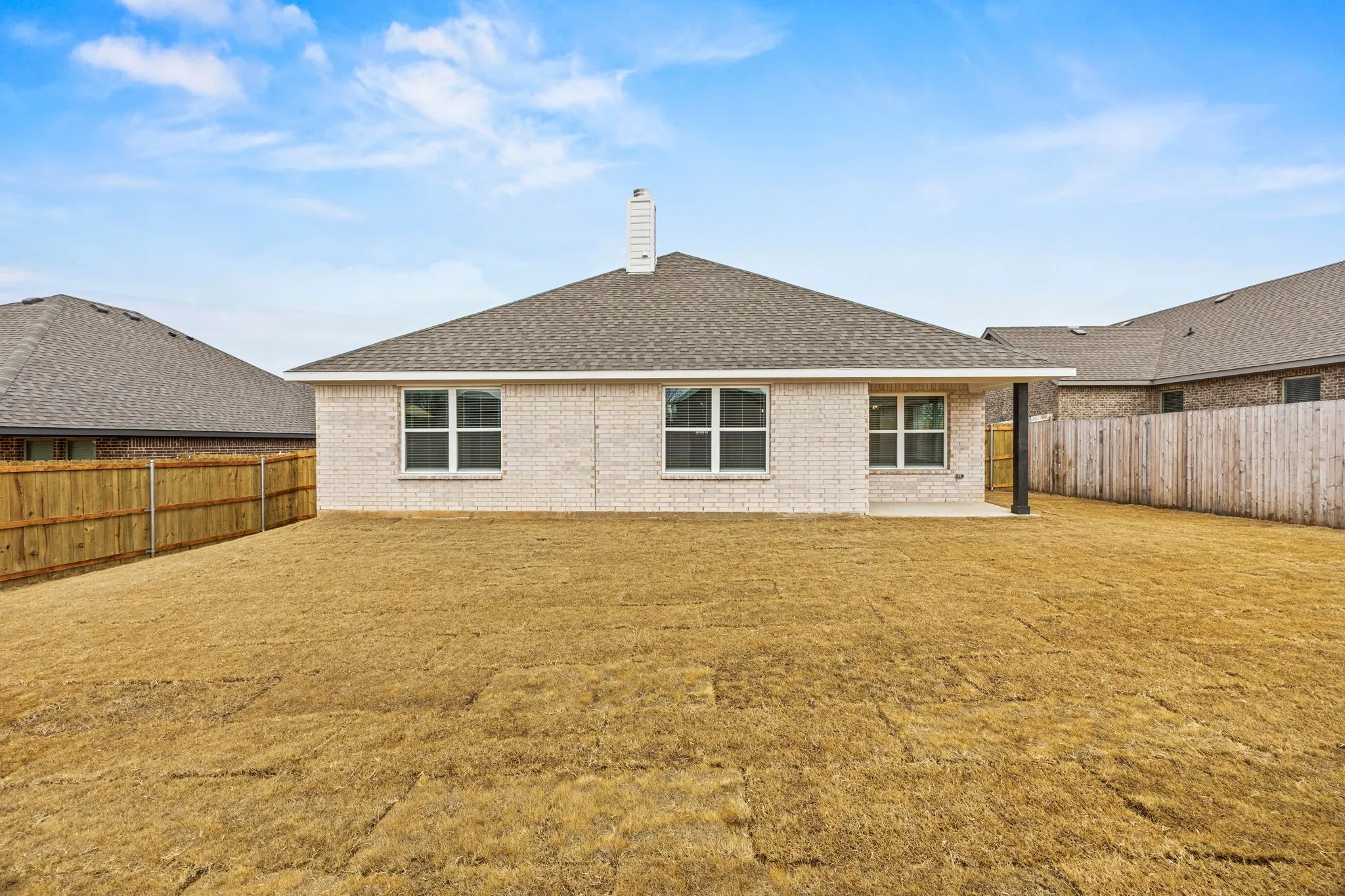 Rear view of house featuring a chimney, a patio, roof with shingles, and a fenced backyard
