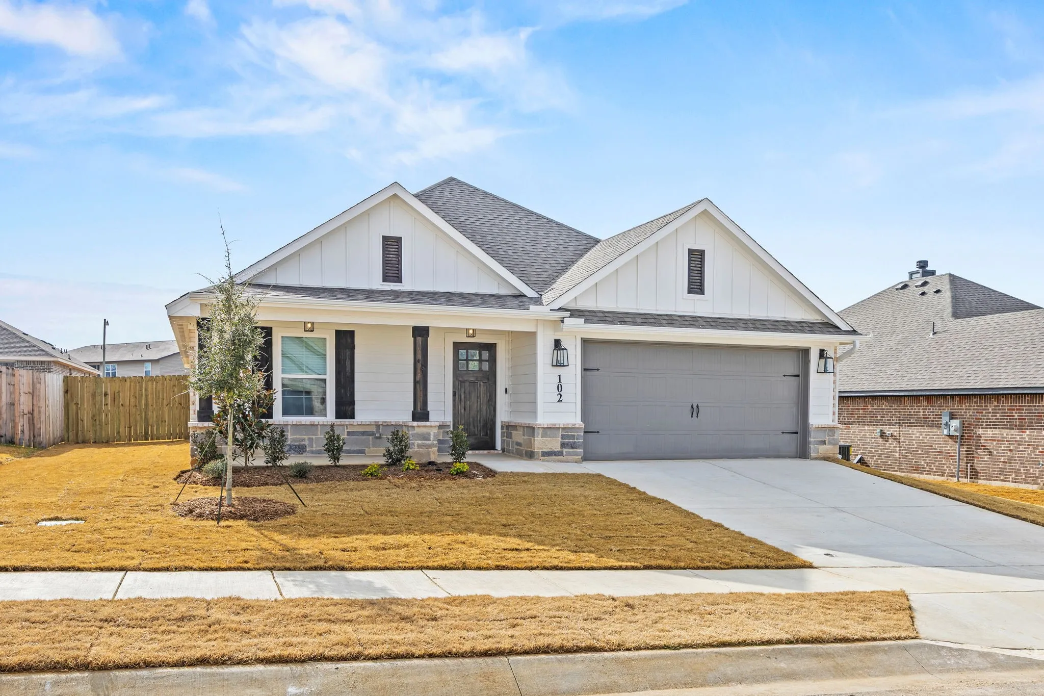 Modern farmhouse style home with board and batten siding, covered porch, roof with shingles, driveway, and stone siding