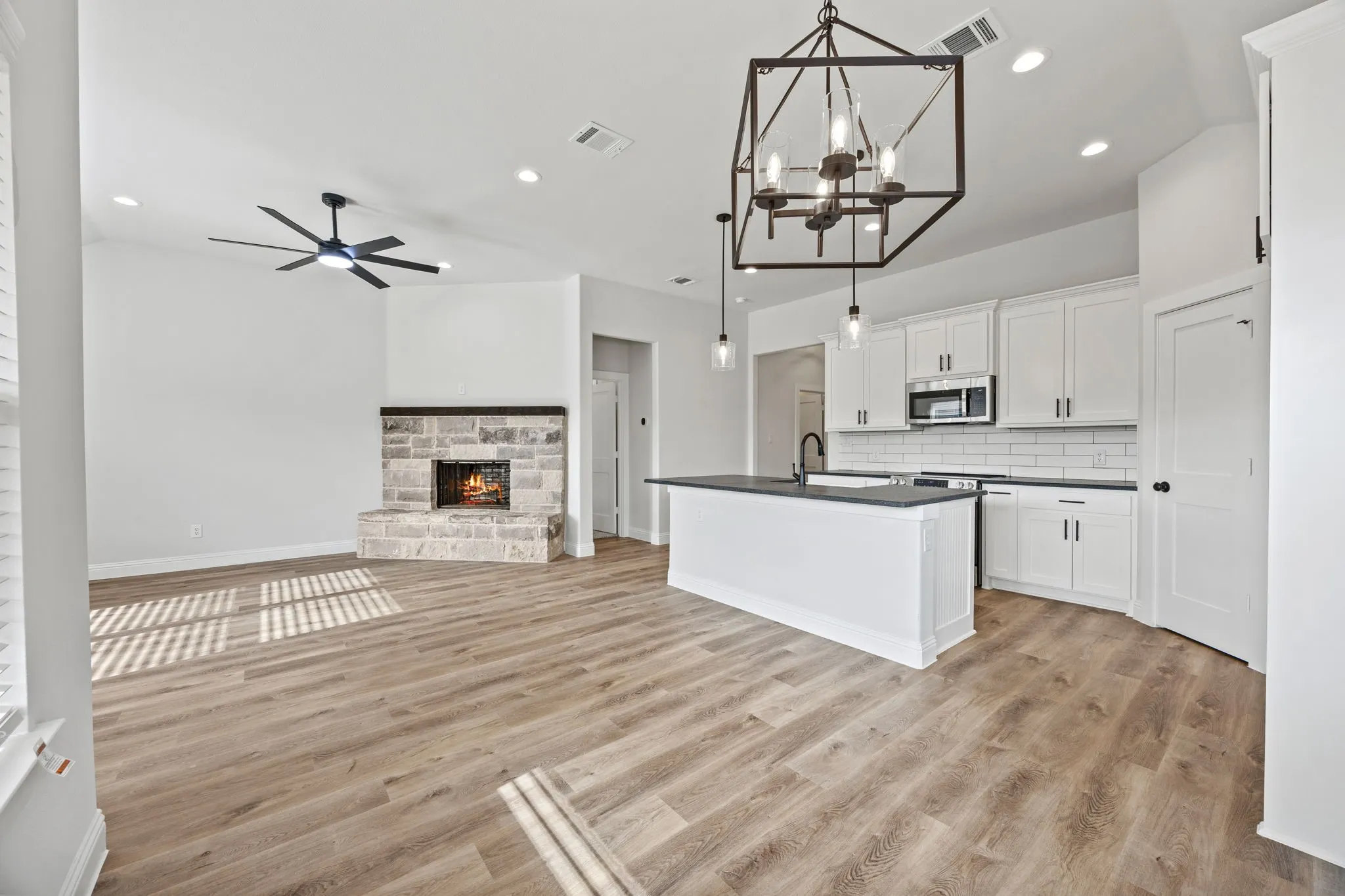 Kitchen featuring open floor plan, white cabinets, a kitchen island with sink, dark countertops, and pendant lighting