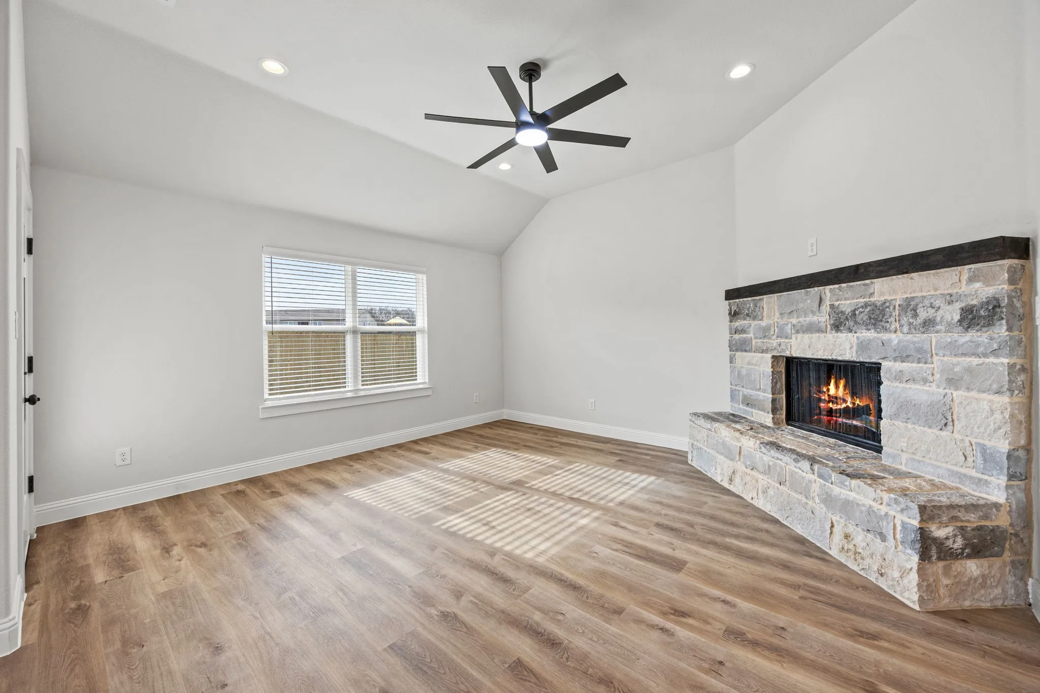 Unfurnished living room featuring vaulted ceiling, recessed lighting, light wood finished floors, a stone fireplace, and ceiling fan