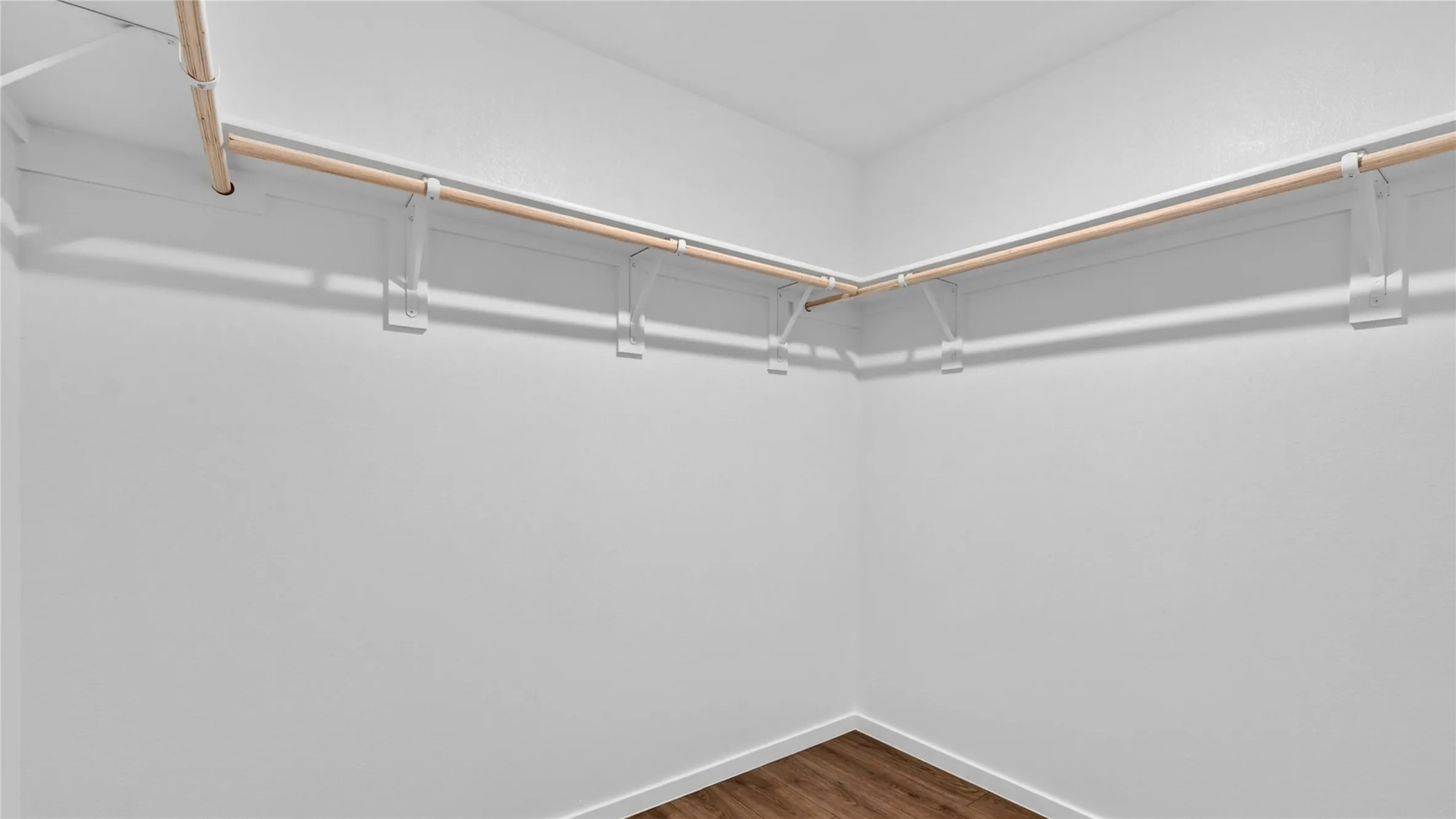 Spacious closet featuring wood-finish flooring, white walls, and built-in shelving with hanging rods
