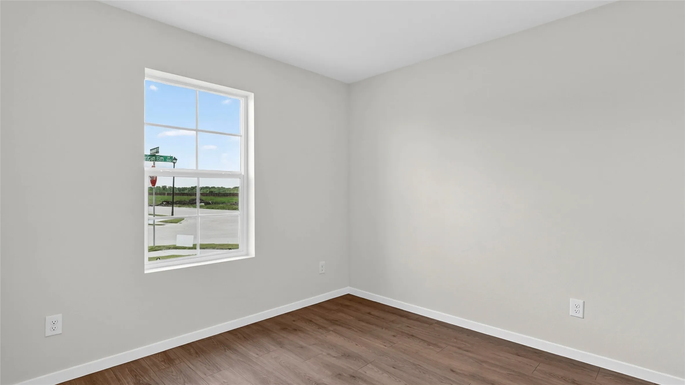 Bright interior room featuring a large grid window, wood-finish flooring, light-toned wall paint, white baseboards, and white trim